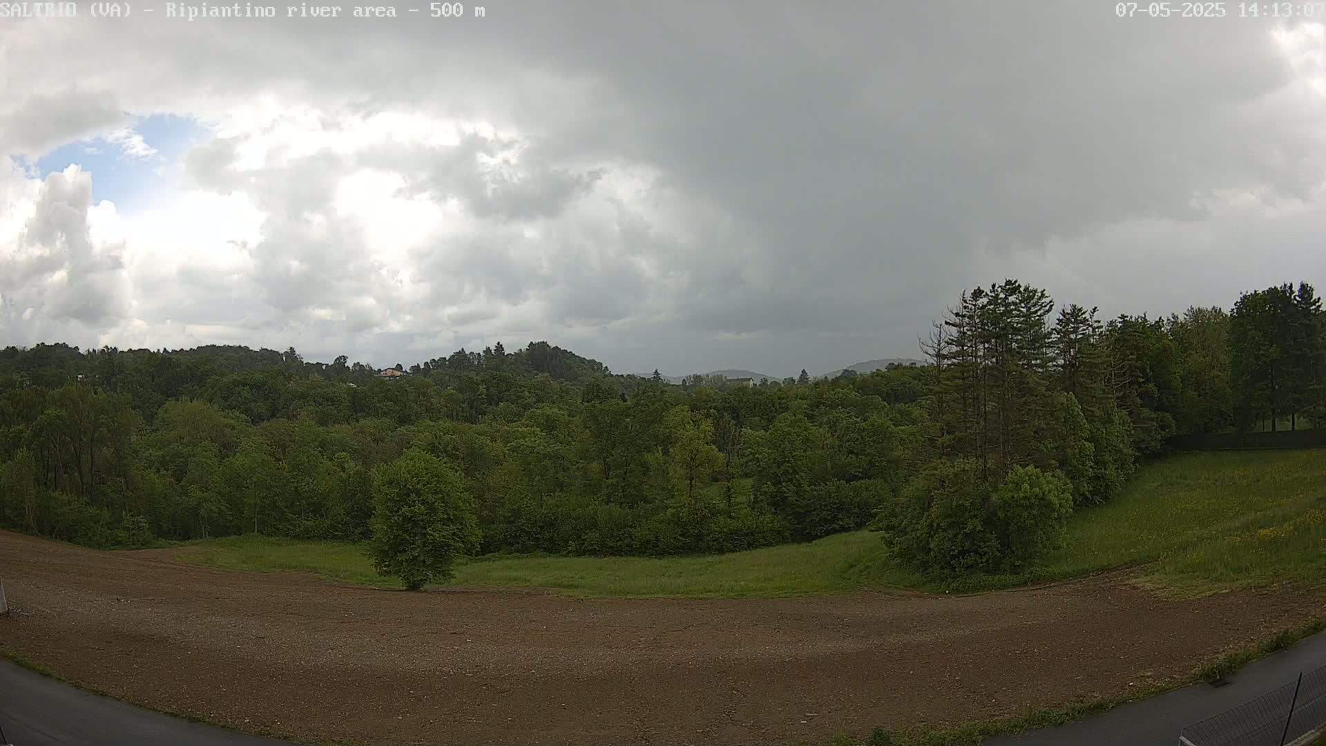A mostly cloudy sky hangs over a verdant landscape of trees and a partially cleared, brown field.