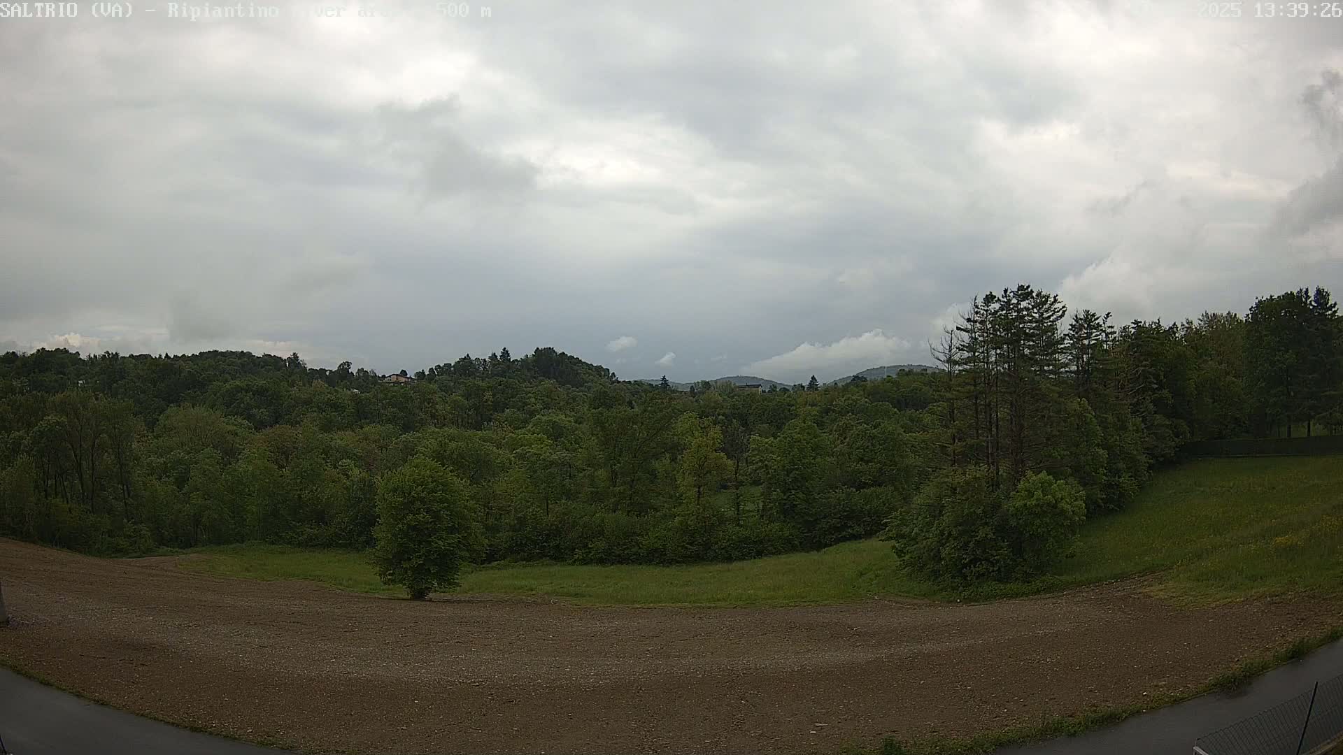 A mostly cloudy sky overlooks a verdant landscape of trees and fields, with a brown, tilled area in the foreground.