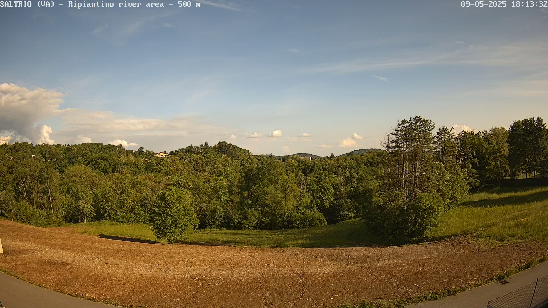 A mostly sunny day reveals a view of a lush green forest and a large, cleared, brown area of land in the foreground.
