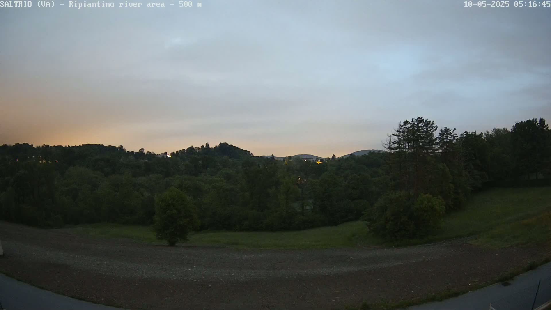 A mostly cloudy, dusky sky over a dark green, tree-covered hillside and a flat, dirt area in the foreground.