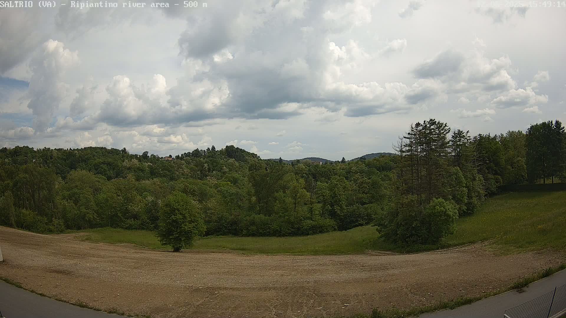 A mostly cloudy sky overlooks a verdant expanse of trees and a flat, barren patch of land.