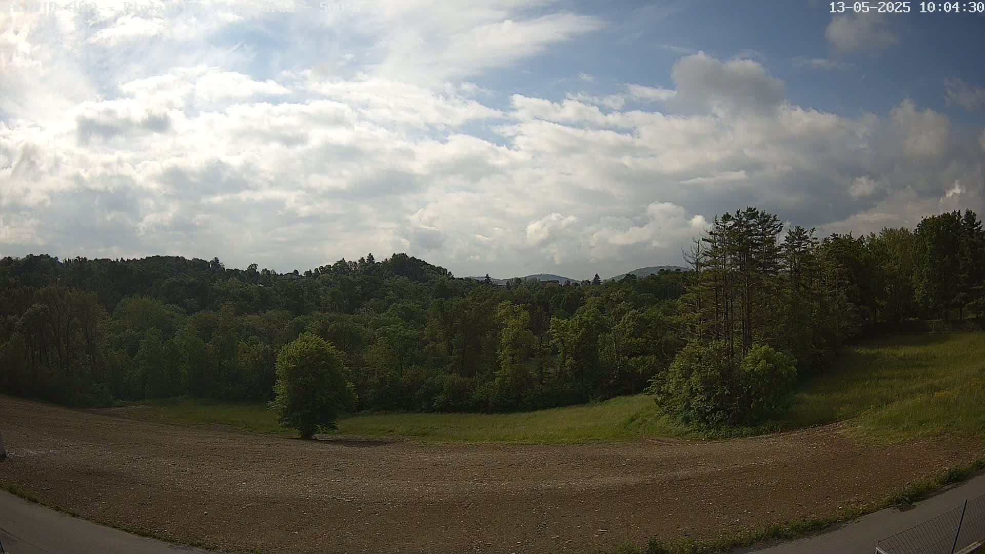 A partly cloudy sky overlooks a mostly-treed landscape with a large, barren, dirt field in the foreground.
