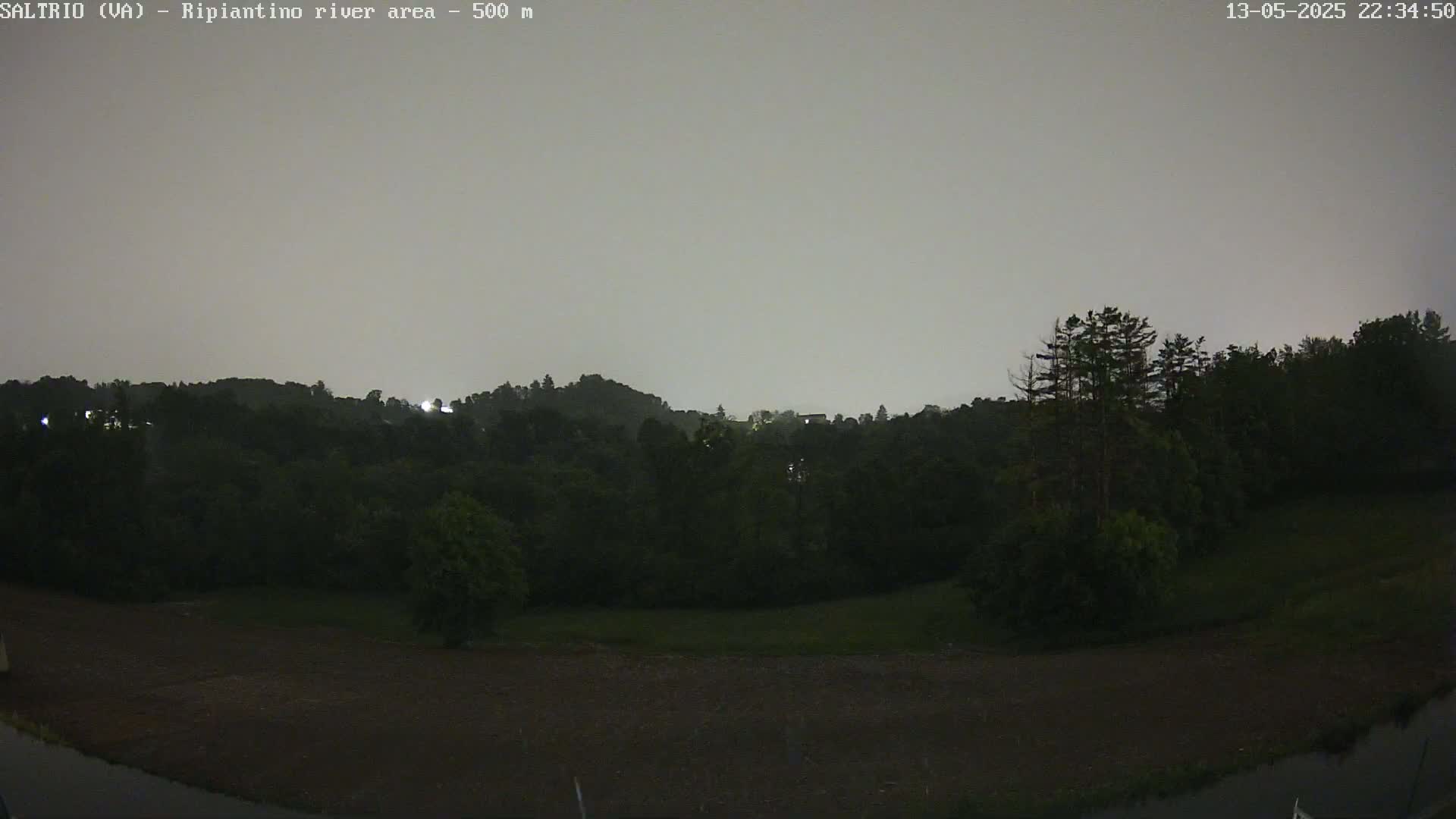 A nighttime view of dark, tree-covered hills under an overcast sky.