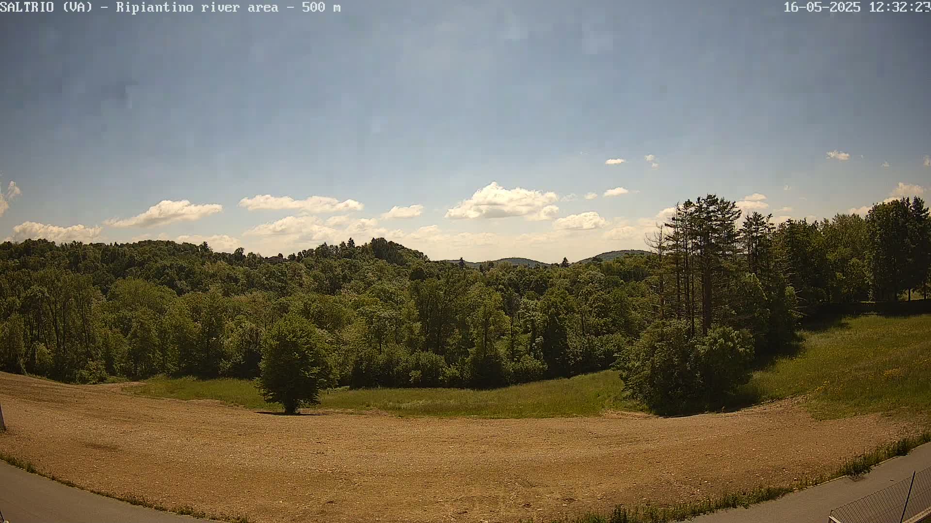 A mostly sunny day shows a view of a mostly treed landscape with a large, bare, dirt area in the foreground.