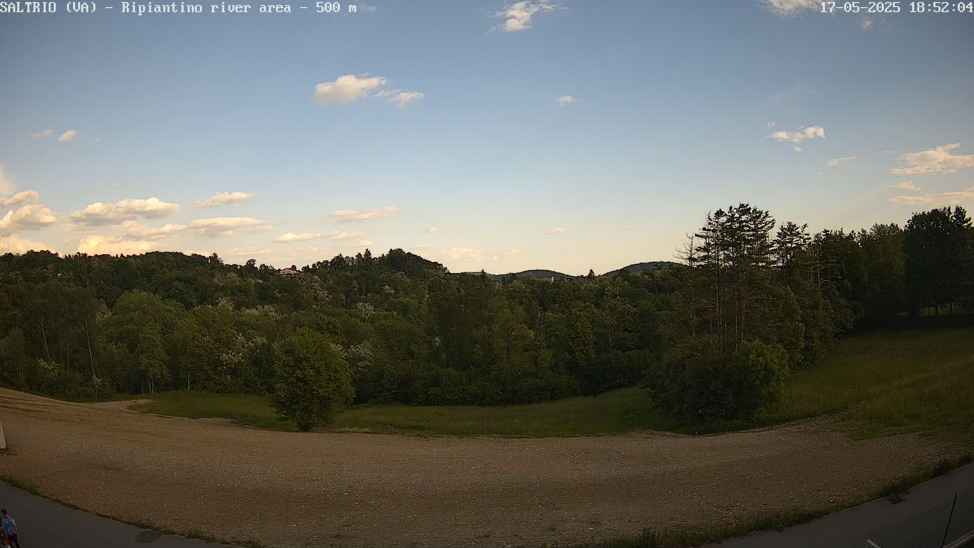 A mostly sunny sky above a landscape of lush green trees and a large, flat, light brown expanse of land.