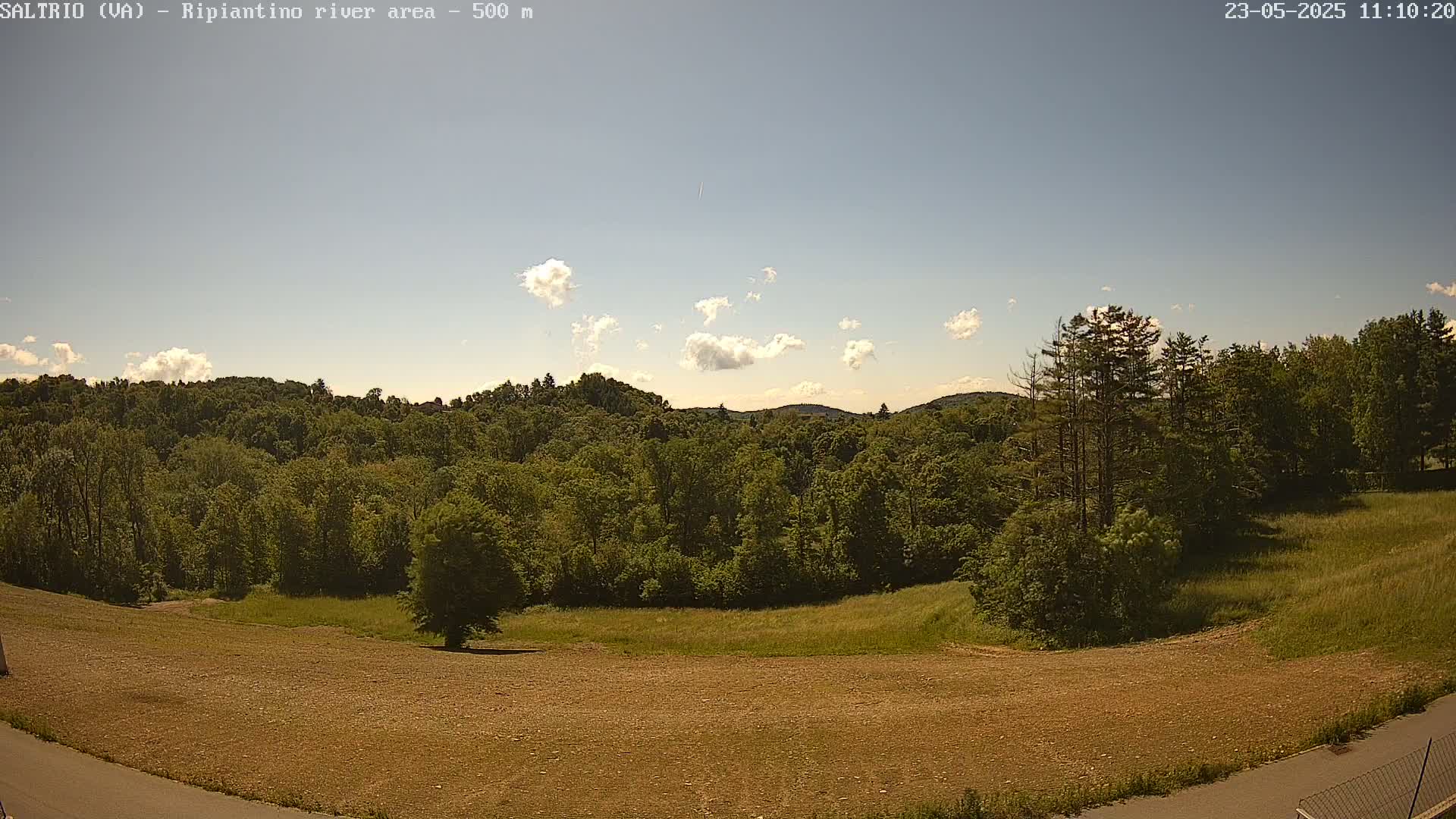 A mostly sunny day reveals a view of a verdant, hilly landscape with a sparsely populated field in the foreground.