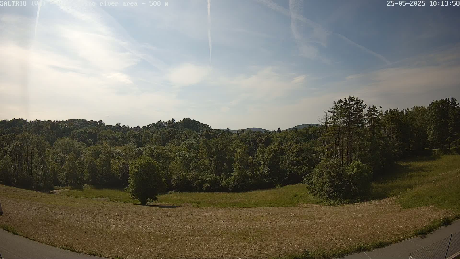 A mostly clear sky overlooks a brown, grassy field next to a lush green forest and distant hills.