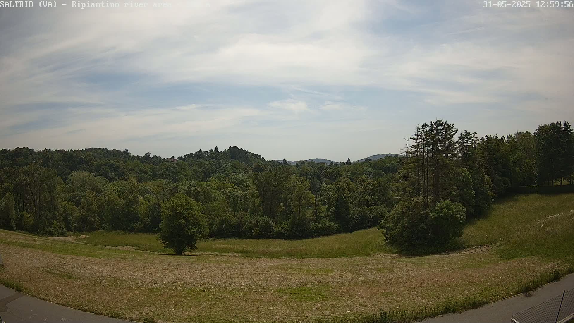 A mostly sunny day reveals a wide expanse of green fields and lush forests, rolling hills in the distance.