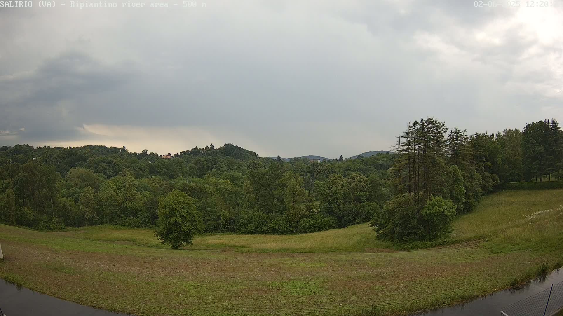 A verdant landscape of fields and forests under a cloudy sky stretches to distant hills.