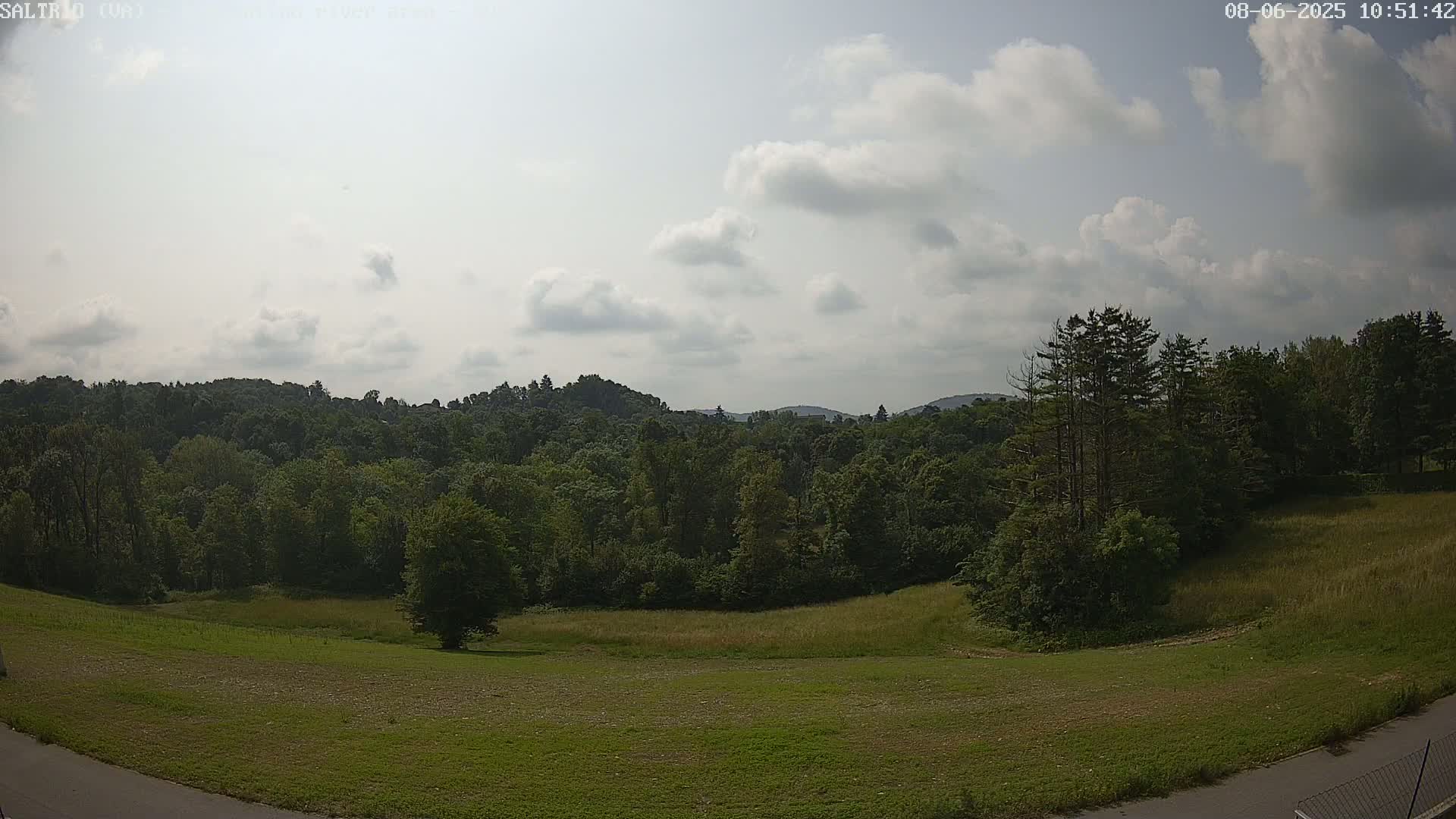 A partly cloudy day reveals a verdant landscape of rolling hills covered in lush green trees and grassy fields.