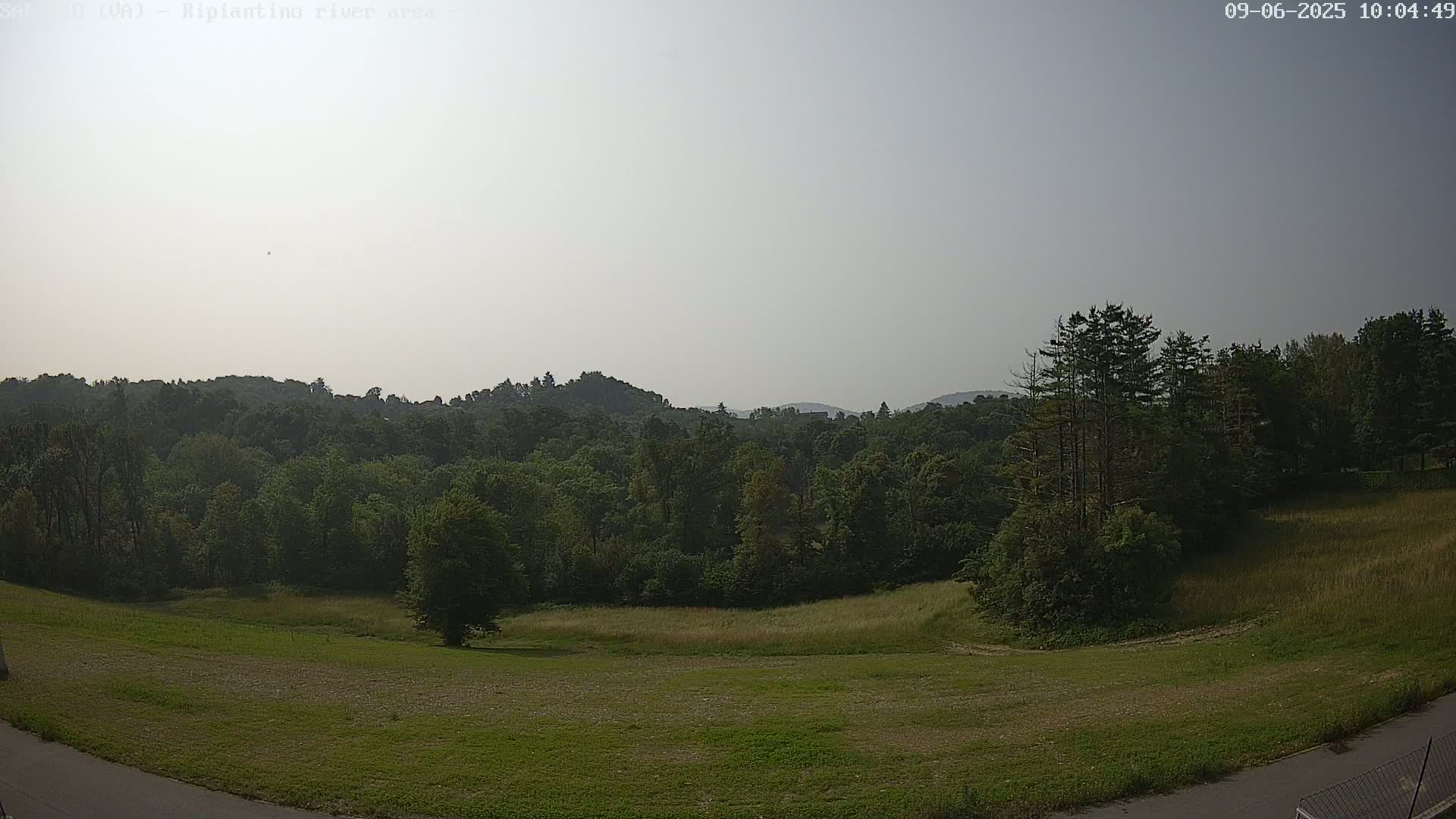 A hazy, sunny day reveals a verdant landscape of grassy fields and lush green forests rolling into distant hills.