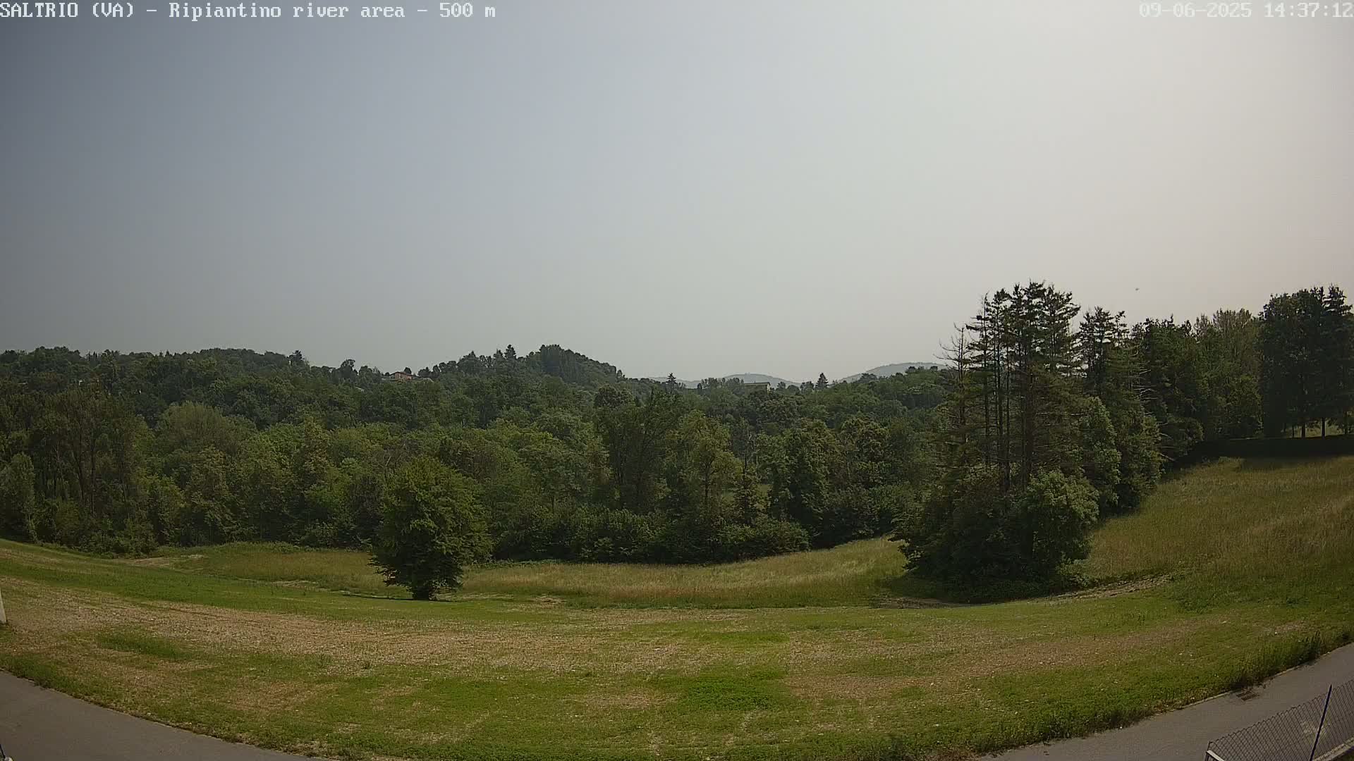 A hazy, sunny day reveals a verdant landscape of rolling hills covered in lush green trees and grassy fields.