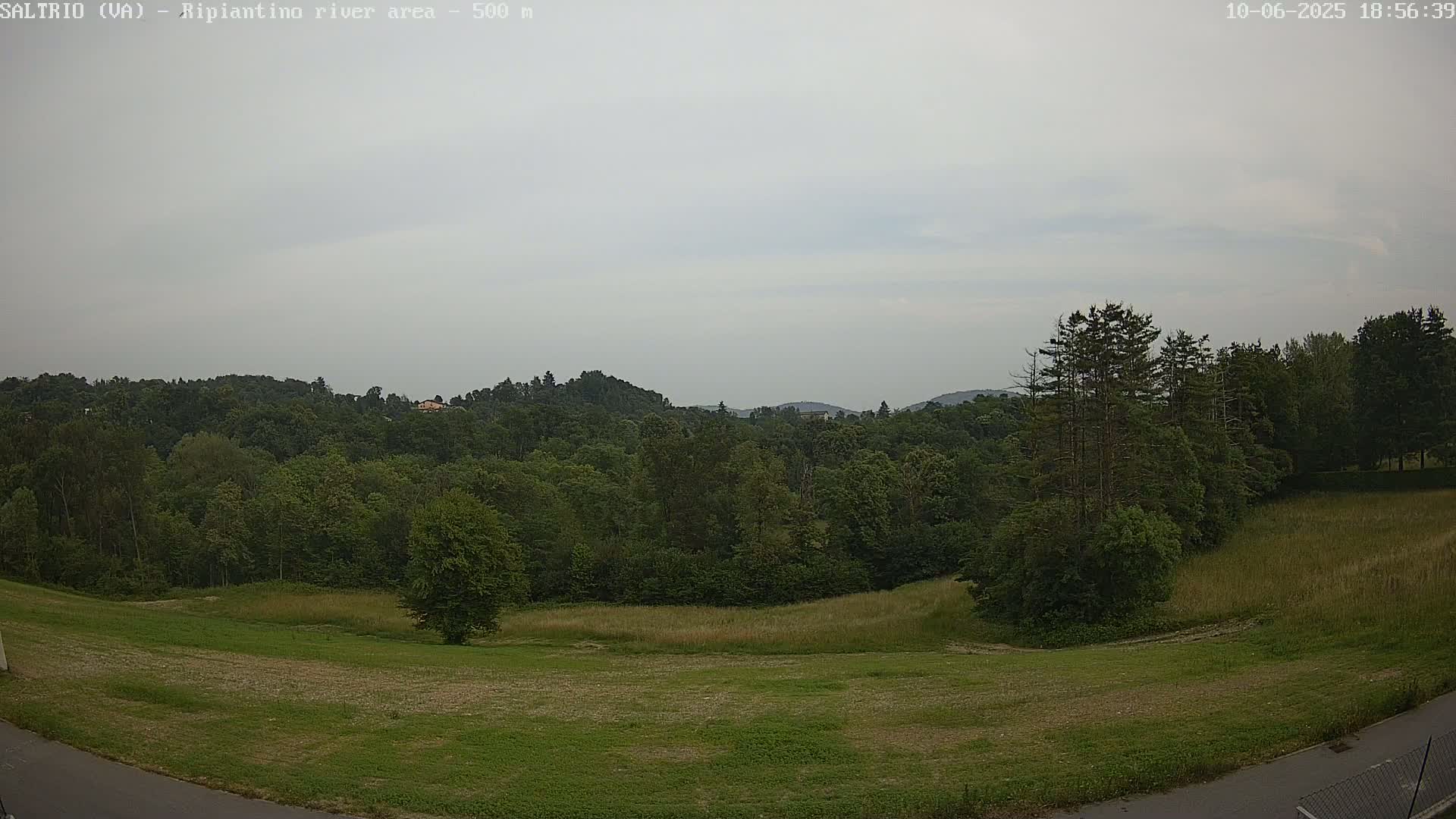A mostly overcast sky over a landscape of green fields and lush forests on a slightly hazy day.