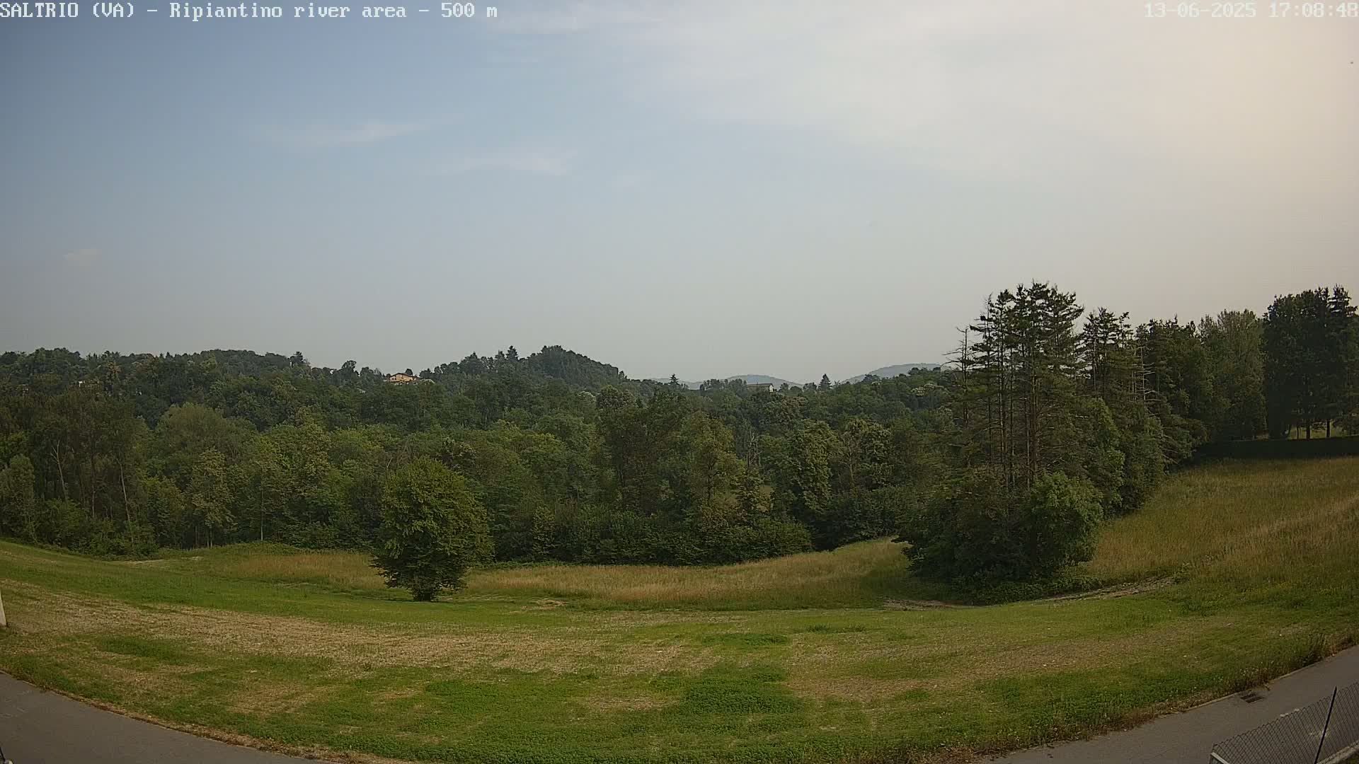 A mostly sunny, hazy day reveals a verdant landscape of grassy fields and lush green forests rolling into distant hills.