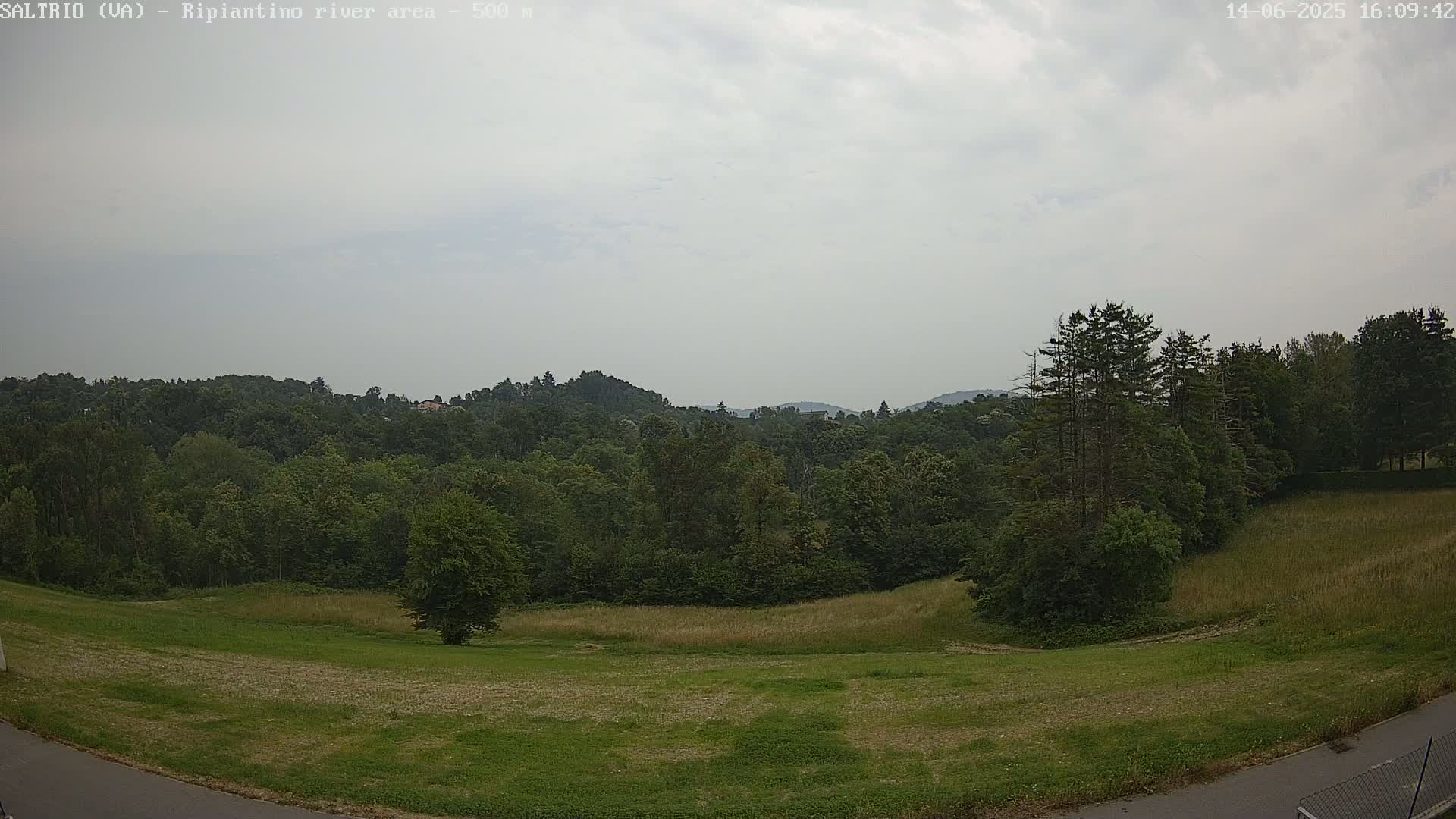 A mostly cloudy sky overlooks a verdant landscape of rolling hills covered in lush green trees and fields.