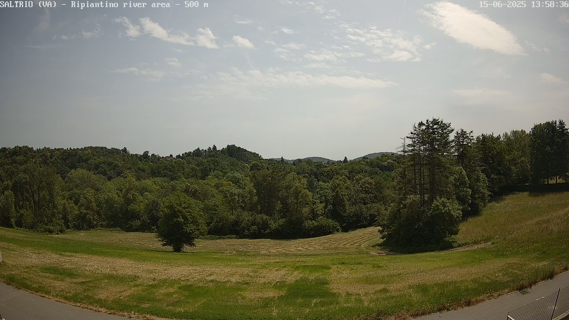A partly sunny day reveals a lush green landscape of trees and a recently mowed field, extending to distant hills under a mostly clear sky.