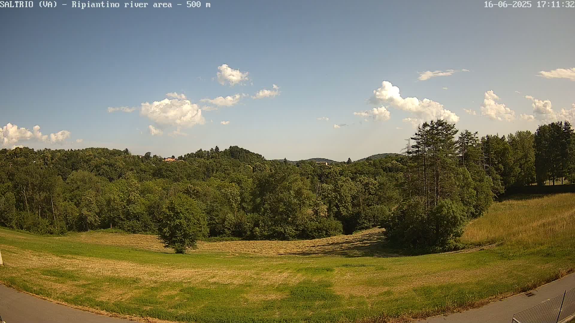 A partly sunny day reveals a lush green landscape of mowed fields and dense forest, rolling hills in the background.