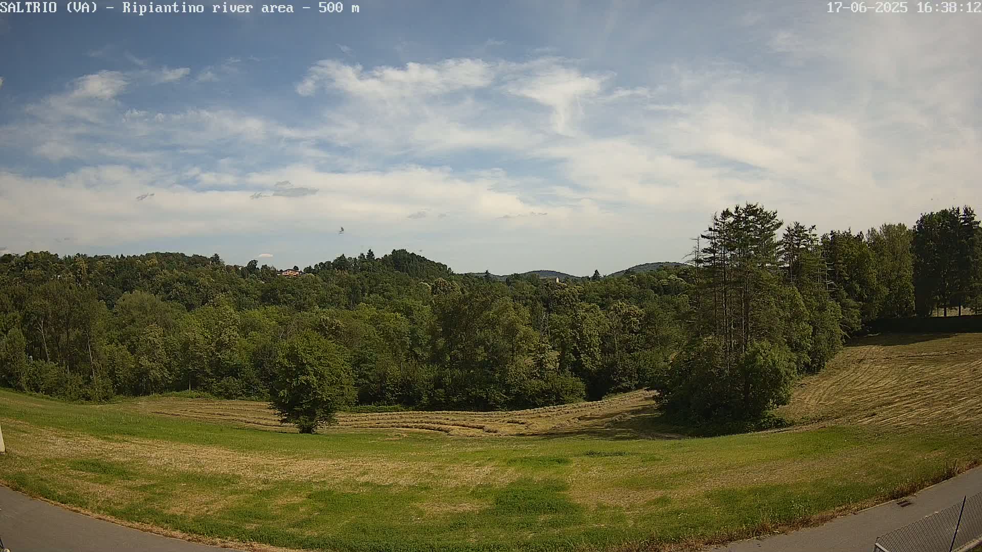 A partly cloudy sky overlooks a lush green landscape of trees and fields, some of which have recently been harvested.