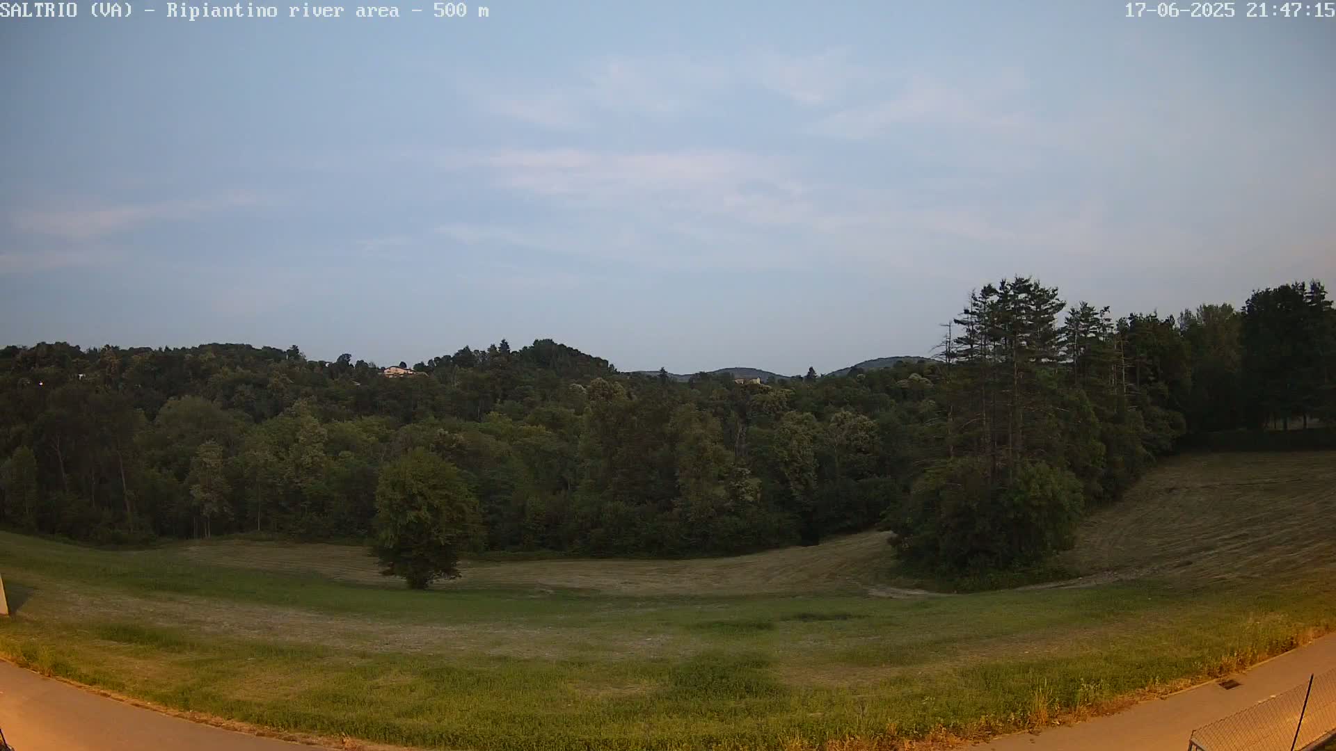 A verdant field and a dense forest, under a mostly clear twilight sky, are visible from a slightly elevated vantage point.