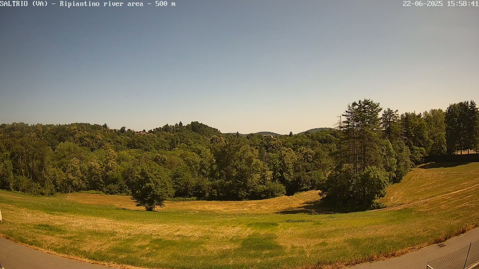 A high-angle view shows a mostly sunny landscape of green and yellow fields and forests under a clear sky.