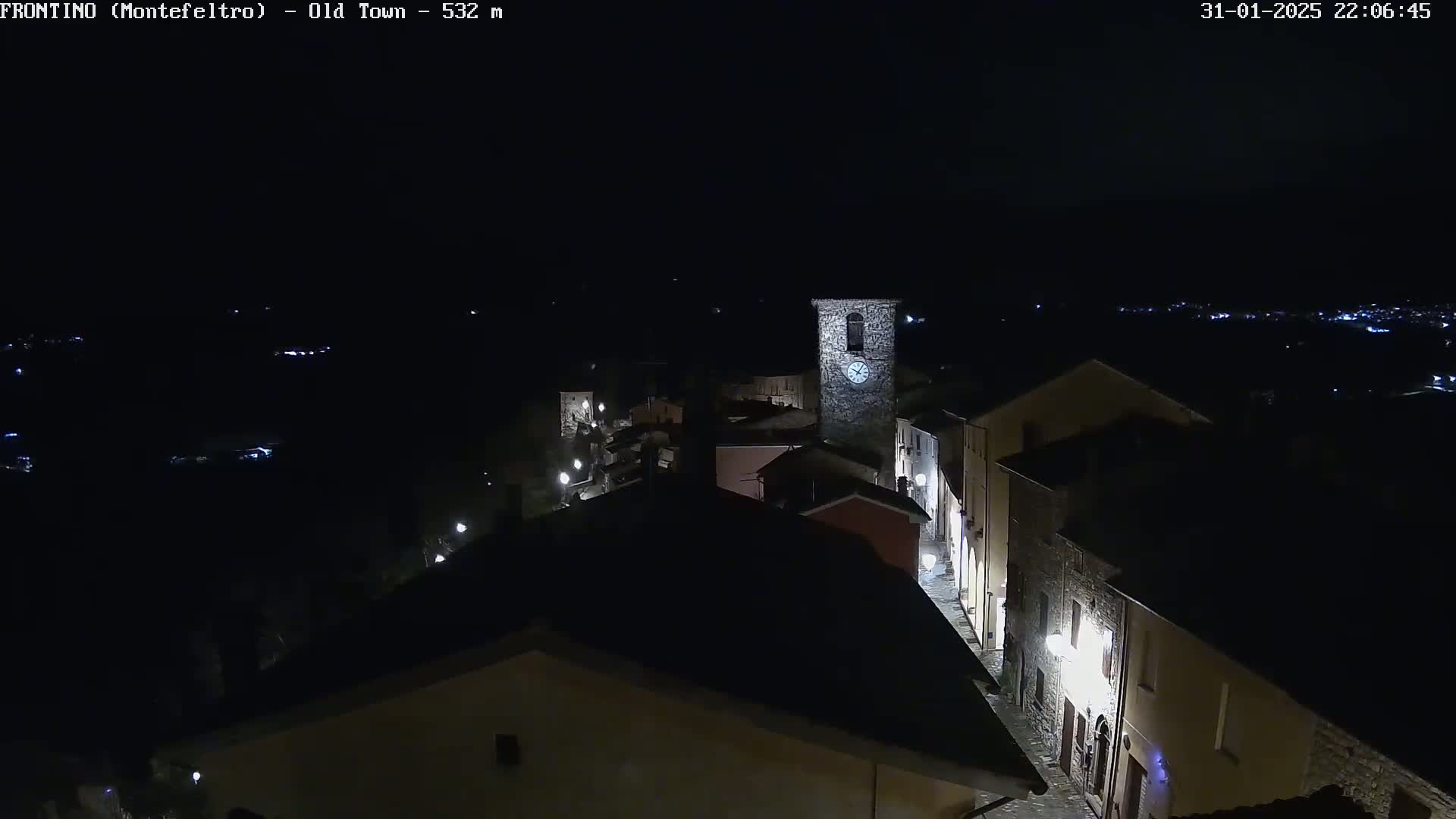 A nighttime, aerial view of a small, dimly lit town with a tall clock tower, under a clear, dark sky.