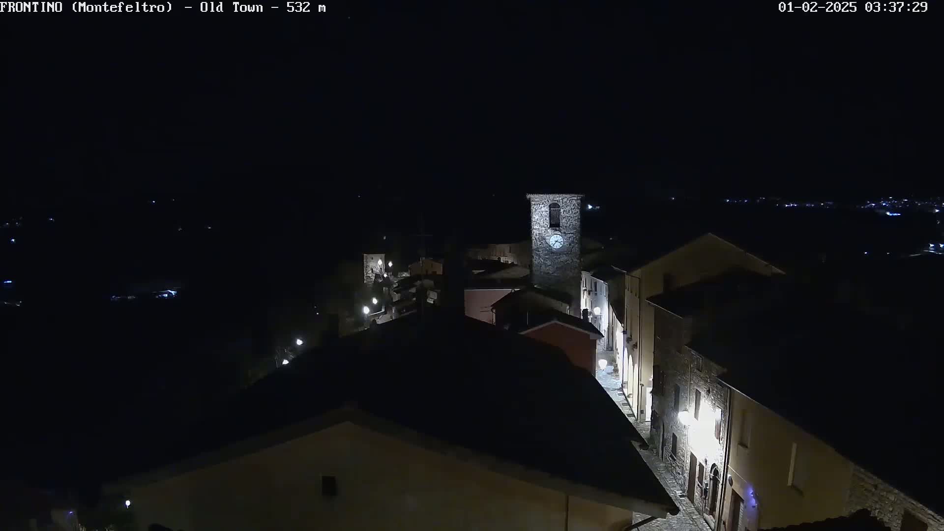 A nighttime, aerial view shows a small, stone village with dimly lit streets and a clock tower.