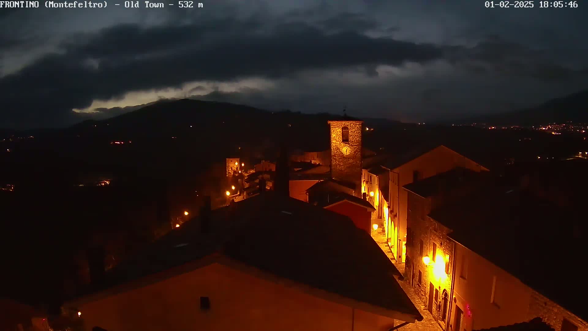 A nighttime view of an illuminated town nestled in a valley under a dark, cloudy sky.