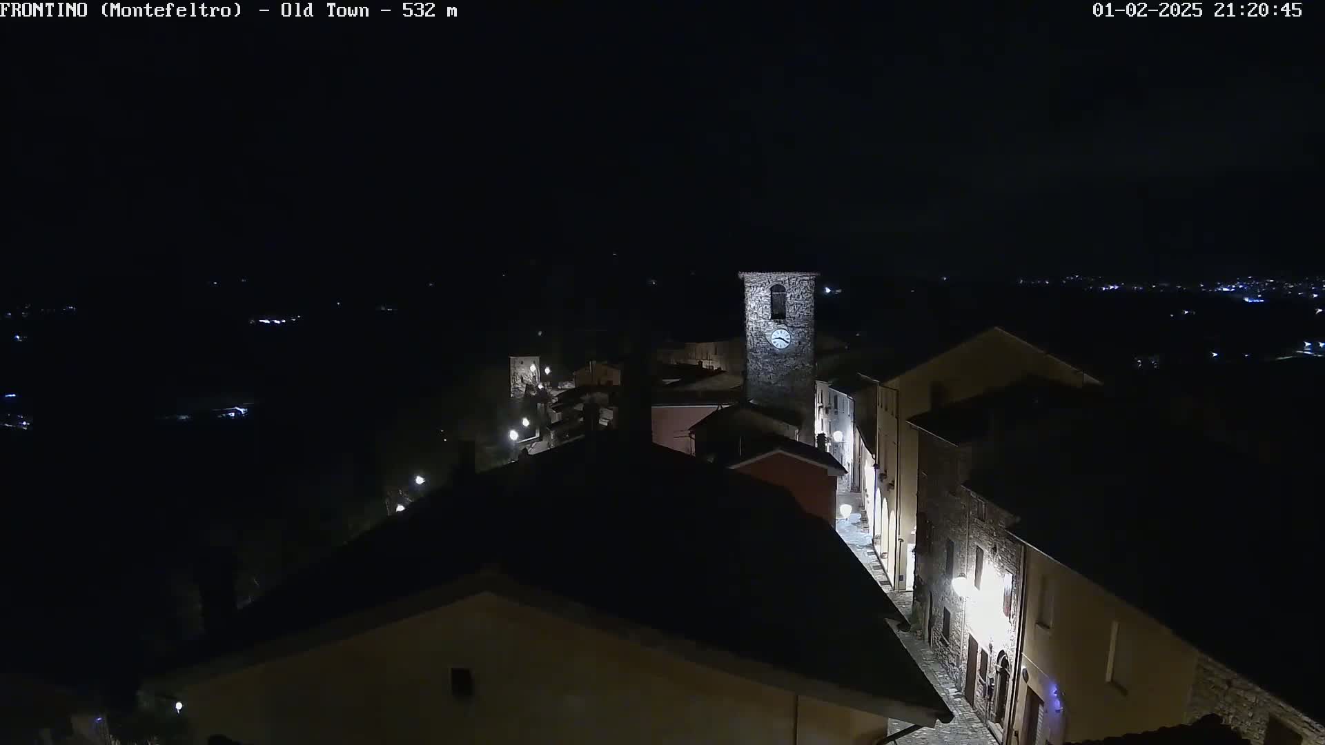 A nighttime, high-angle view of a dimly lit old town with a clock tower, surrounded by darkness.