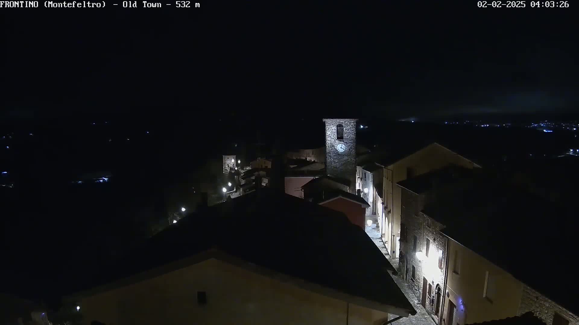 A nighttime, high-angle view of a small, dimly lit town with a clock tower, under a dark sky.