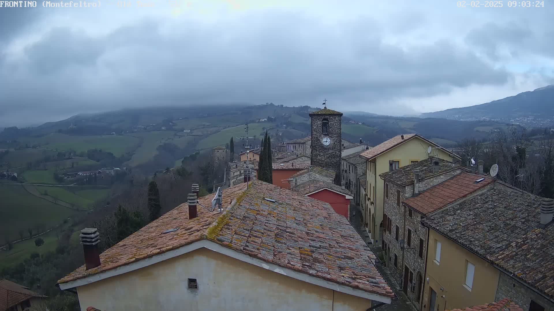 A view from a rooftop shows a small town nestled in a valley under a cloudy sky.