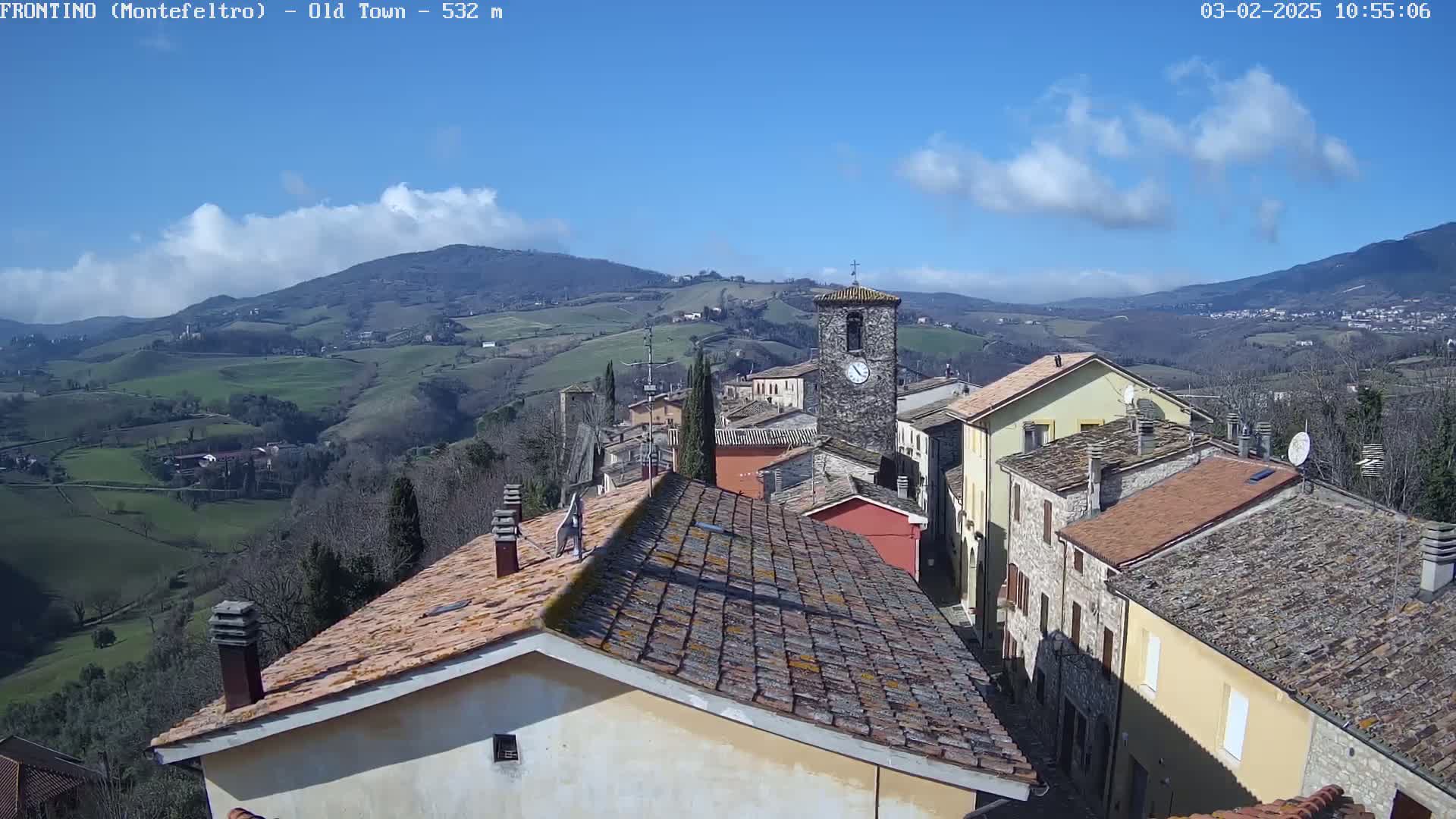 A view of a small town nestled in a hilly landscape under a mostly sunny sky with some clouds.