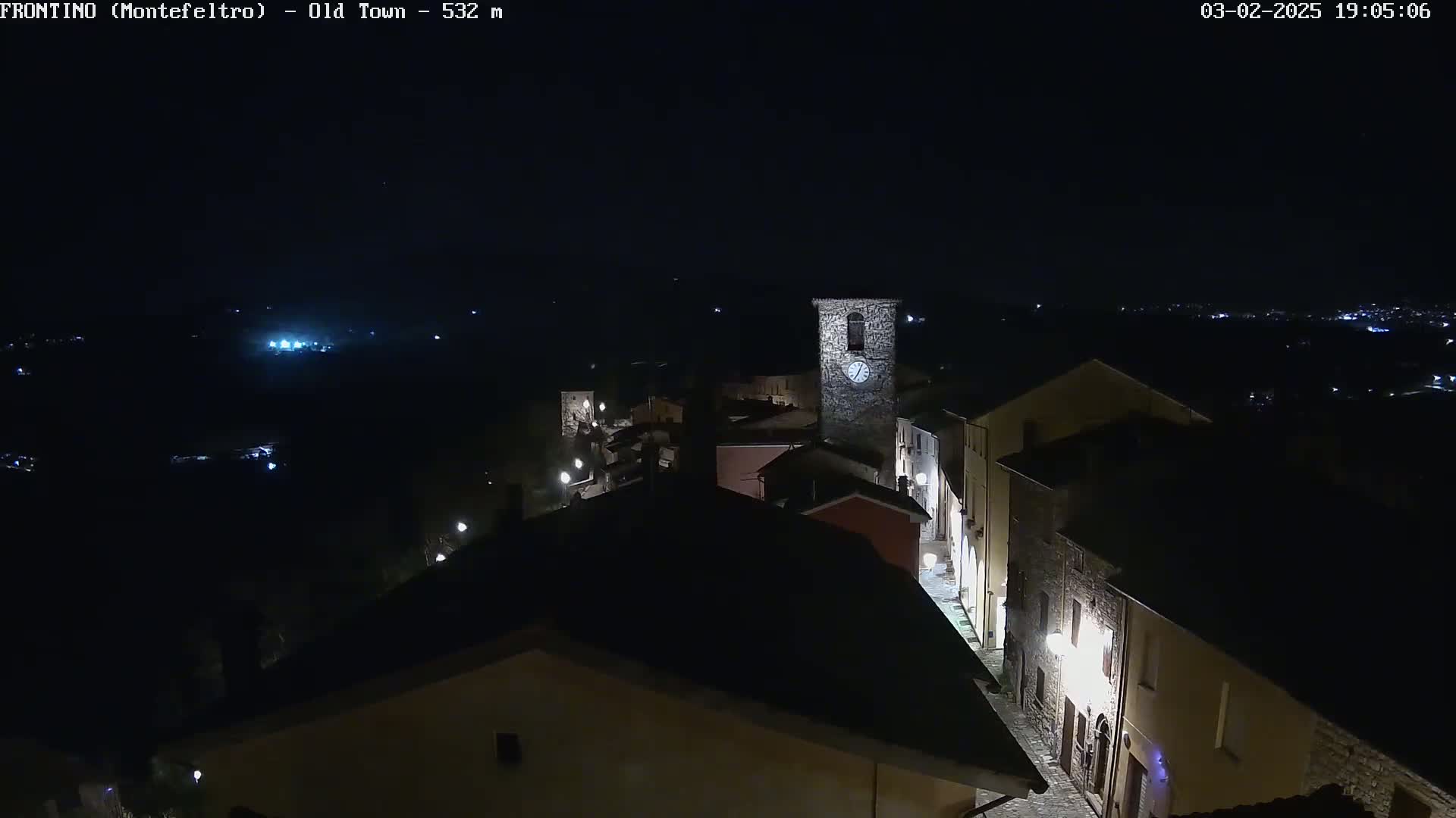 A nighttime, aerial view of a small, dimly lit town with a clock tower, under a clear, dark sky.
