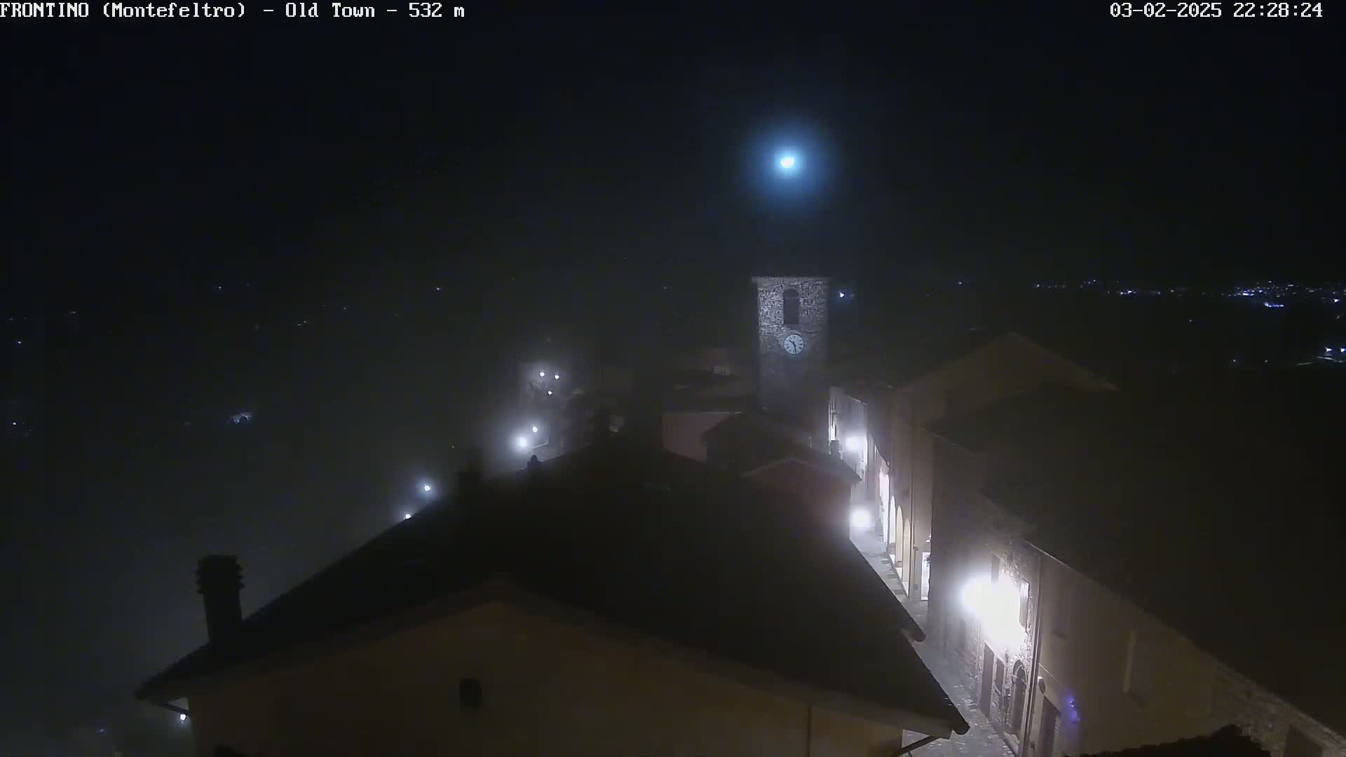 A foggy night scene shows a dimly lit old town with a clock tower, viewed from above.