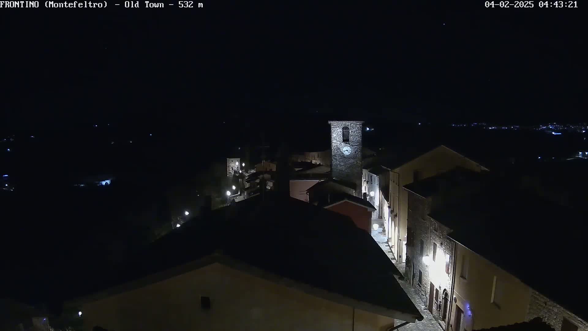 A nighttime, aerial view of a small town with dimly lit buildings and a clock tower, under a clear, dark sky.