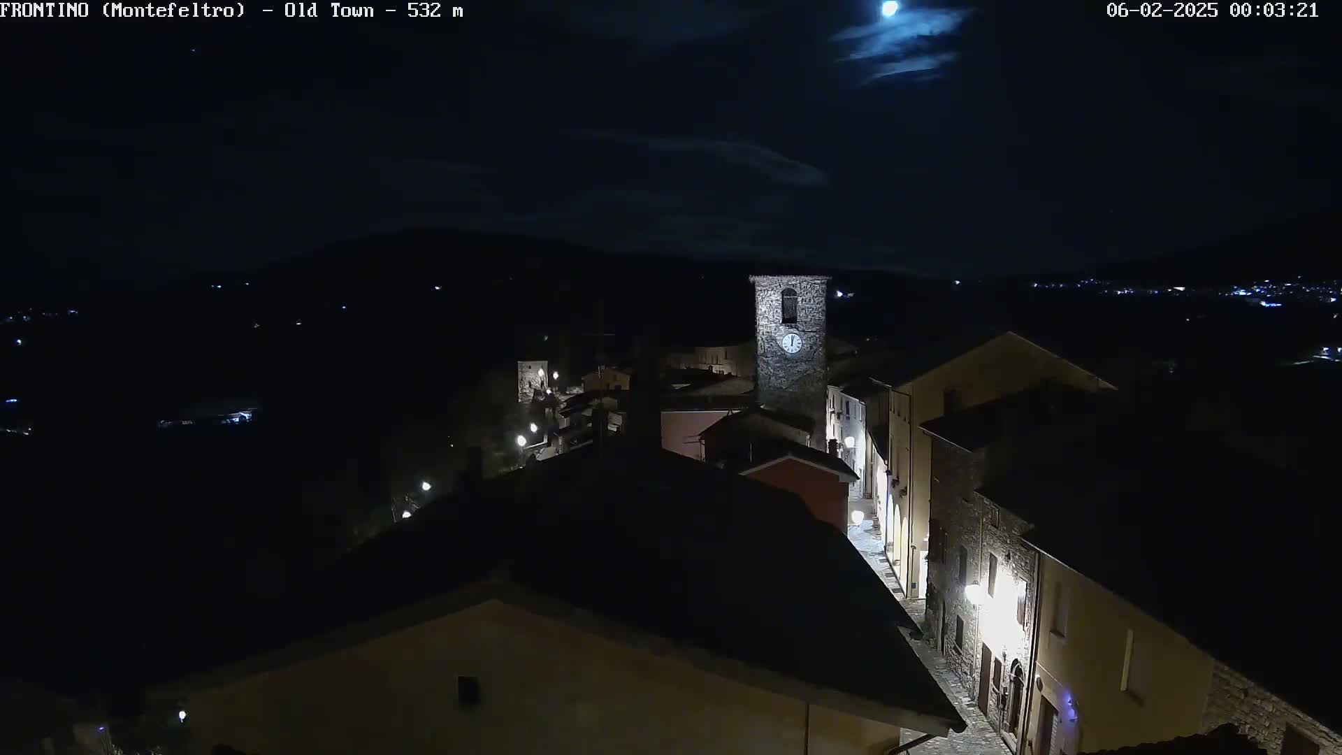 A nighttime, overhead view of a small town with a clock tower, under a mostly clear sky with a bright moon.