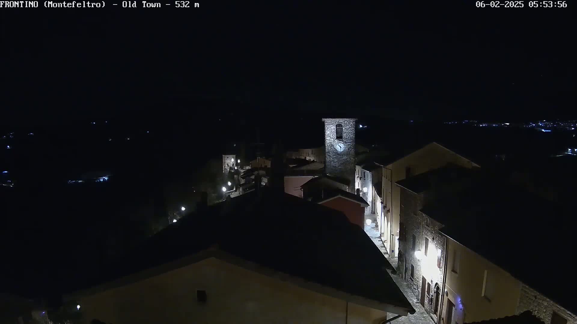 A nighttime, aerial view shows a small, dimly lit town with a clock tower, under a clear, dark sky.