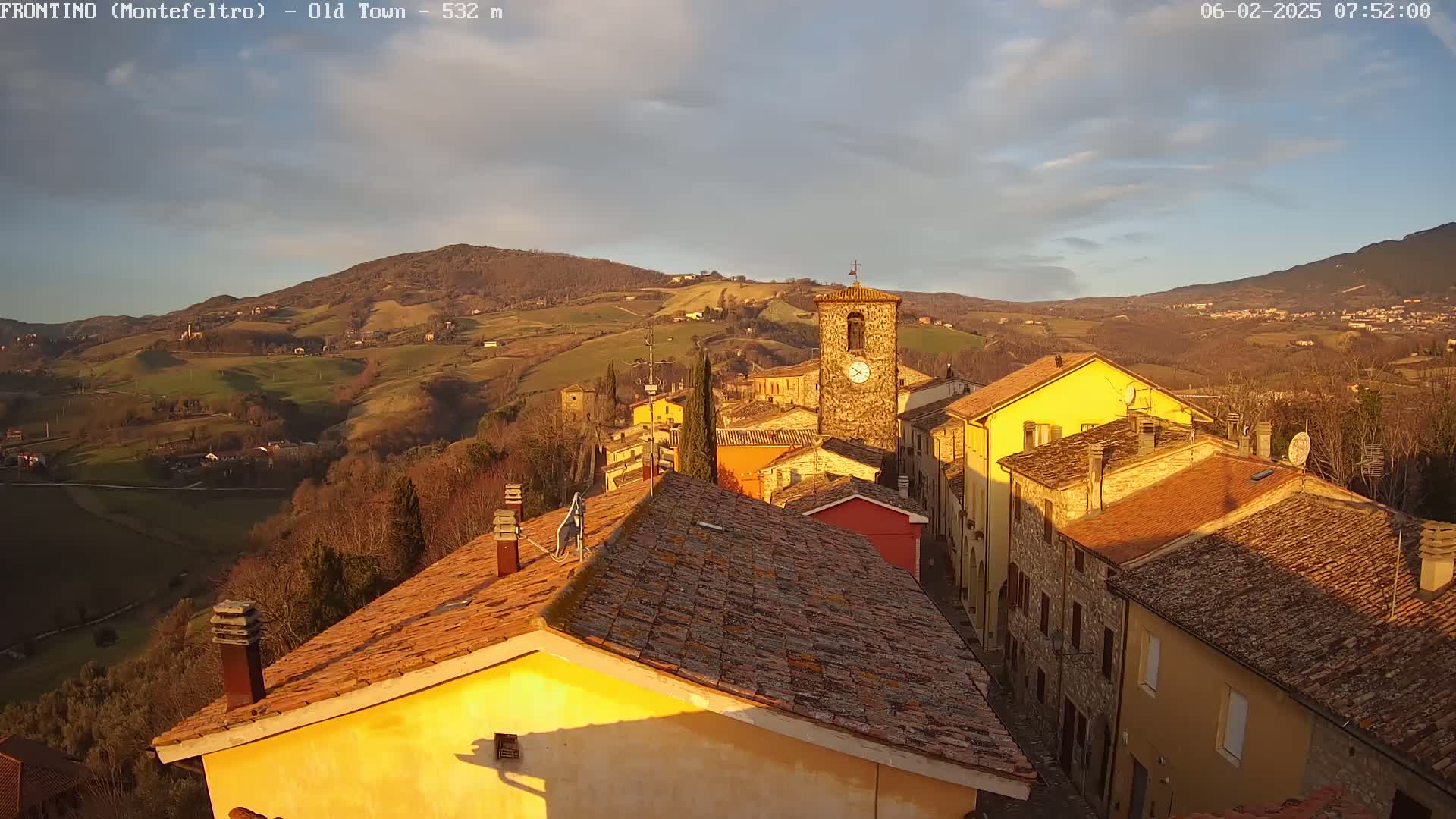 A quaint village nestled in rolling hills under a partly cloudy, golden-hued sunset sky.