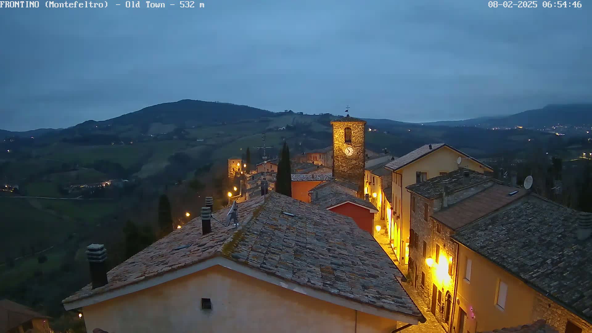 A small, dimly lit town nestled in rolling hills under a twilight sky.