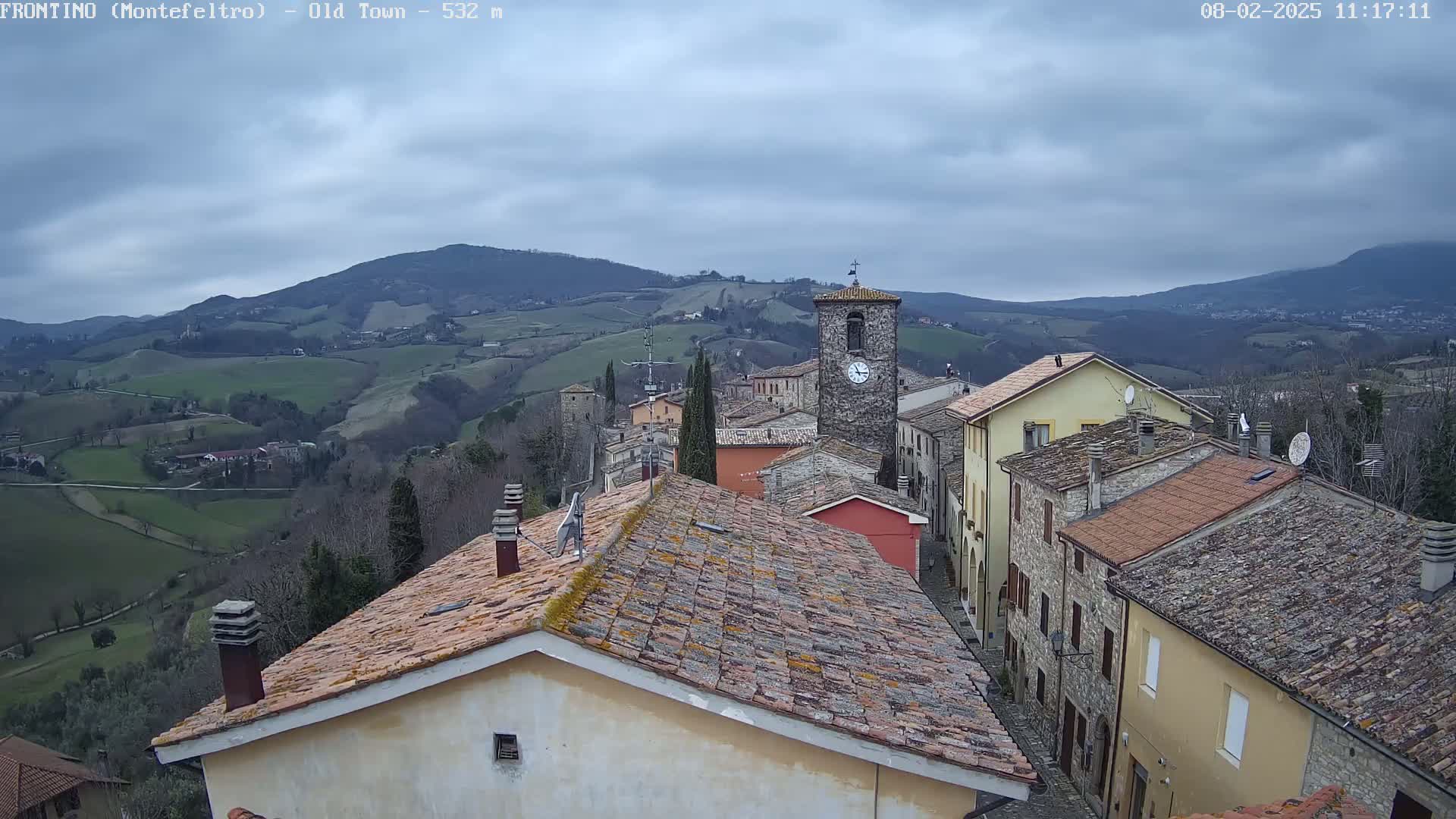 A view from a rooftop shows an overcast day over a small town nestled in a valley between rolling hills.