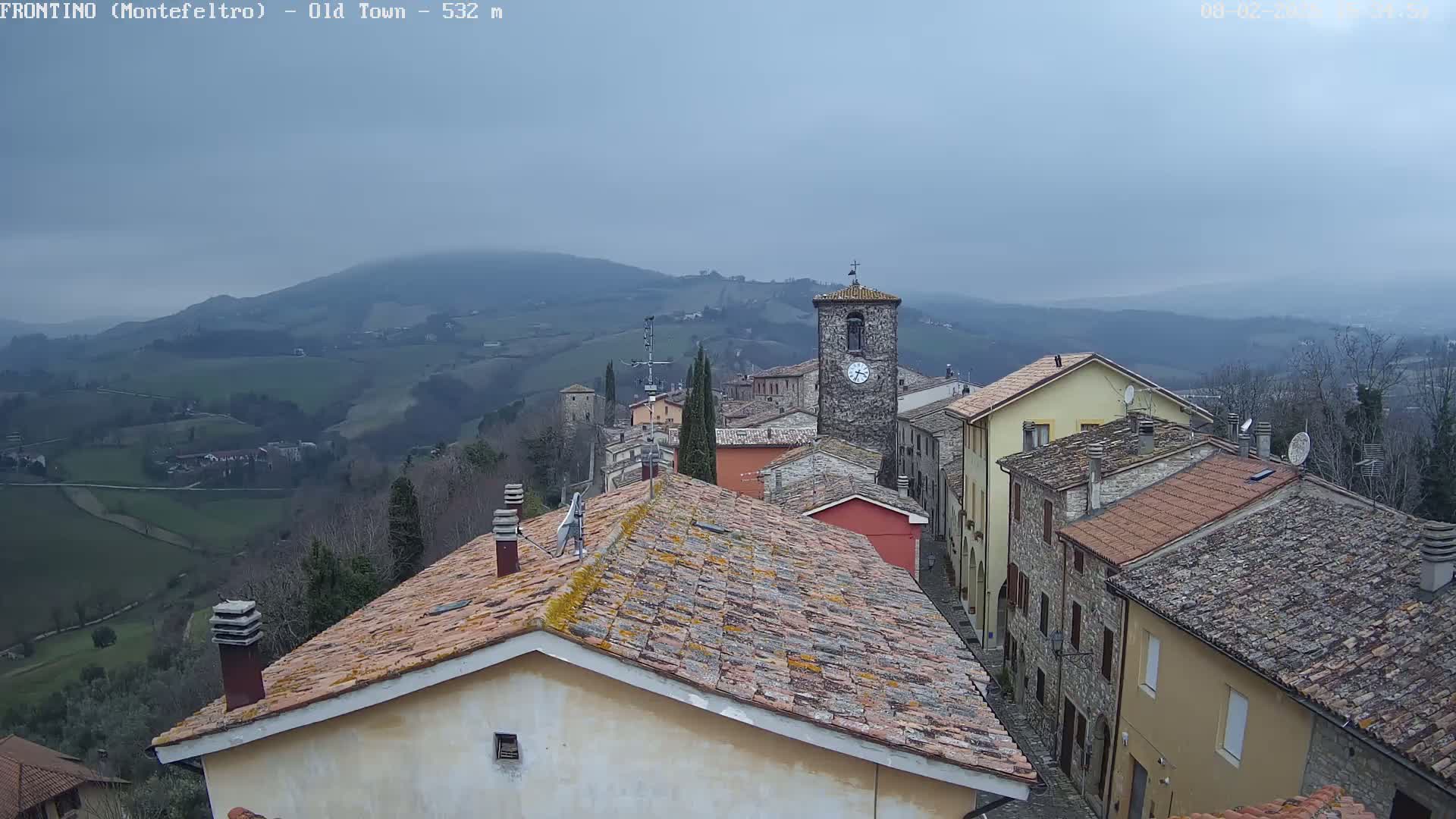 A view from a rooftop shows a small town nestled in a valley under an overcast sky.