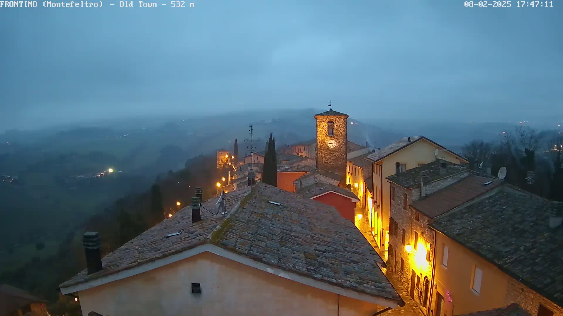 A dimly lit, hilly town with a clock tower is shrouded in a misty twilight.