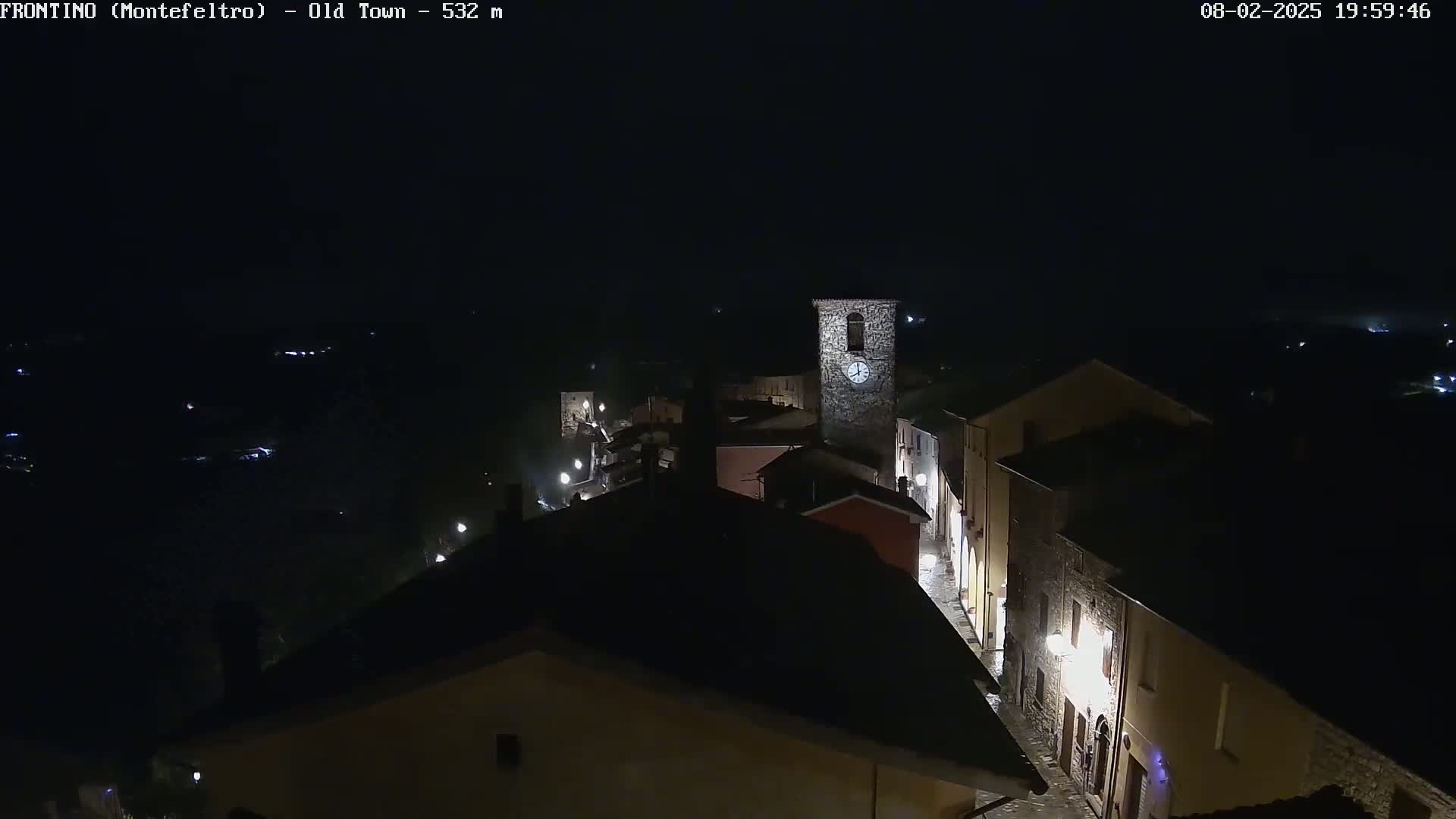 A nighttime, high-angle view shows a small town with dimly lit stone buildings and a clock tower.
