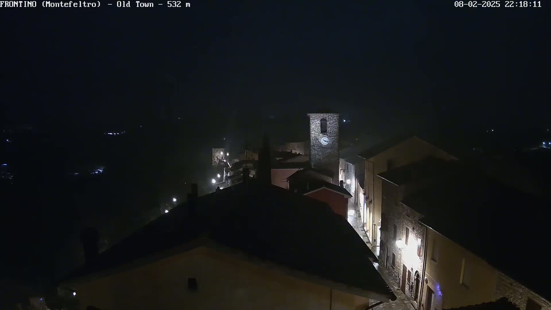 A nighttime, foggy view of a small town with a clock tower, showing dimly lit buildings and streets.