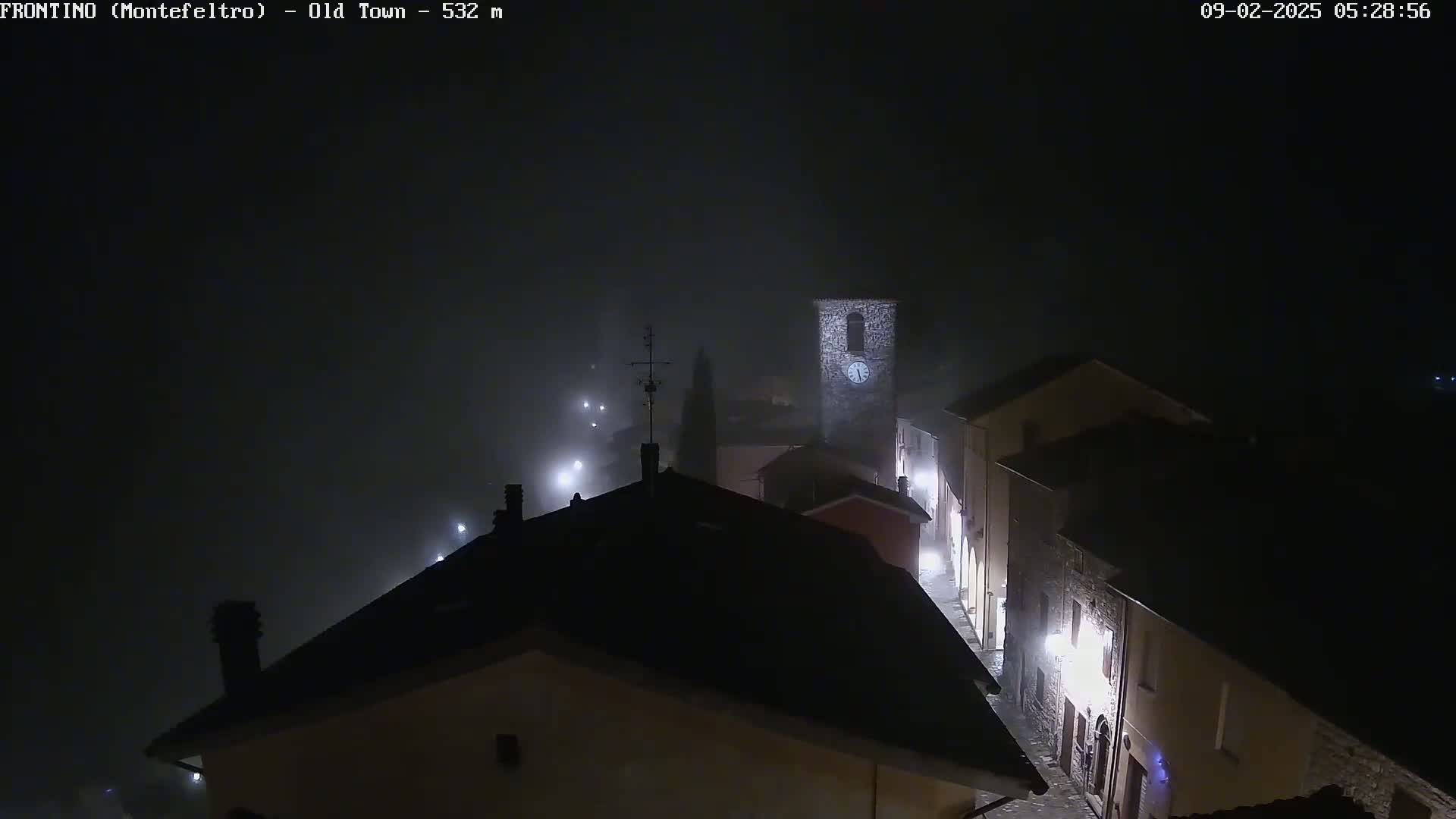 A foggy night scene shows a dimly lit old town with stone buildings and a clock tower.