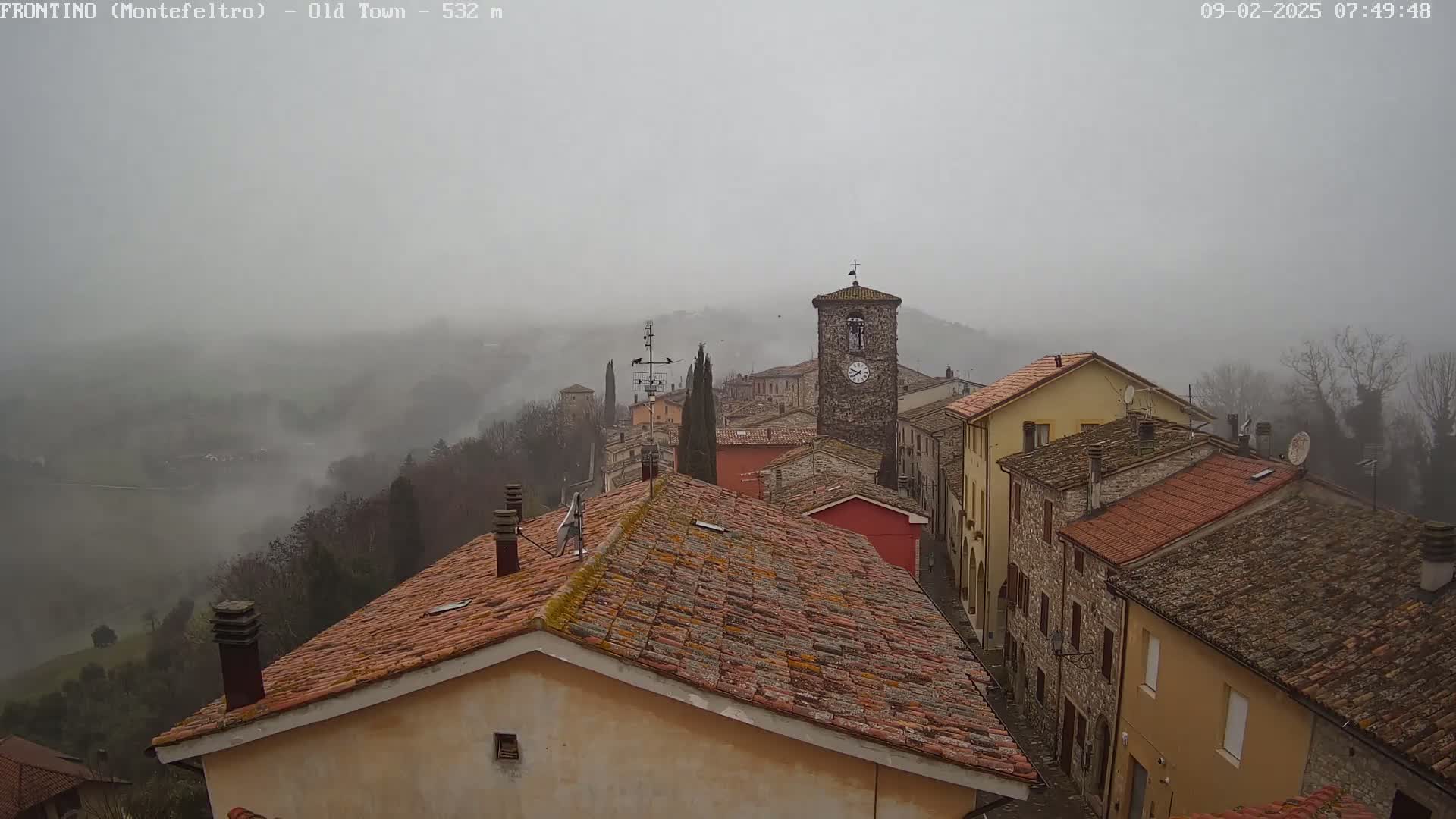 A foggy, overcast view of a small town nestled in a valley, showing rooftops and a clock tower.