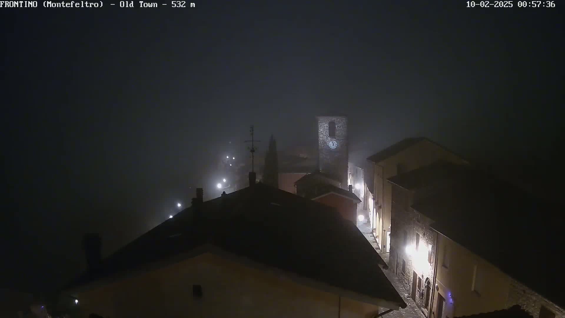 A foggy night scene shows a small town with dimly lit buildings and a tall stone tower.