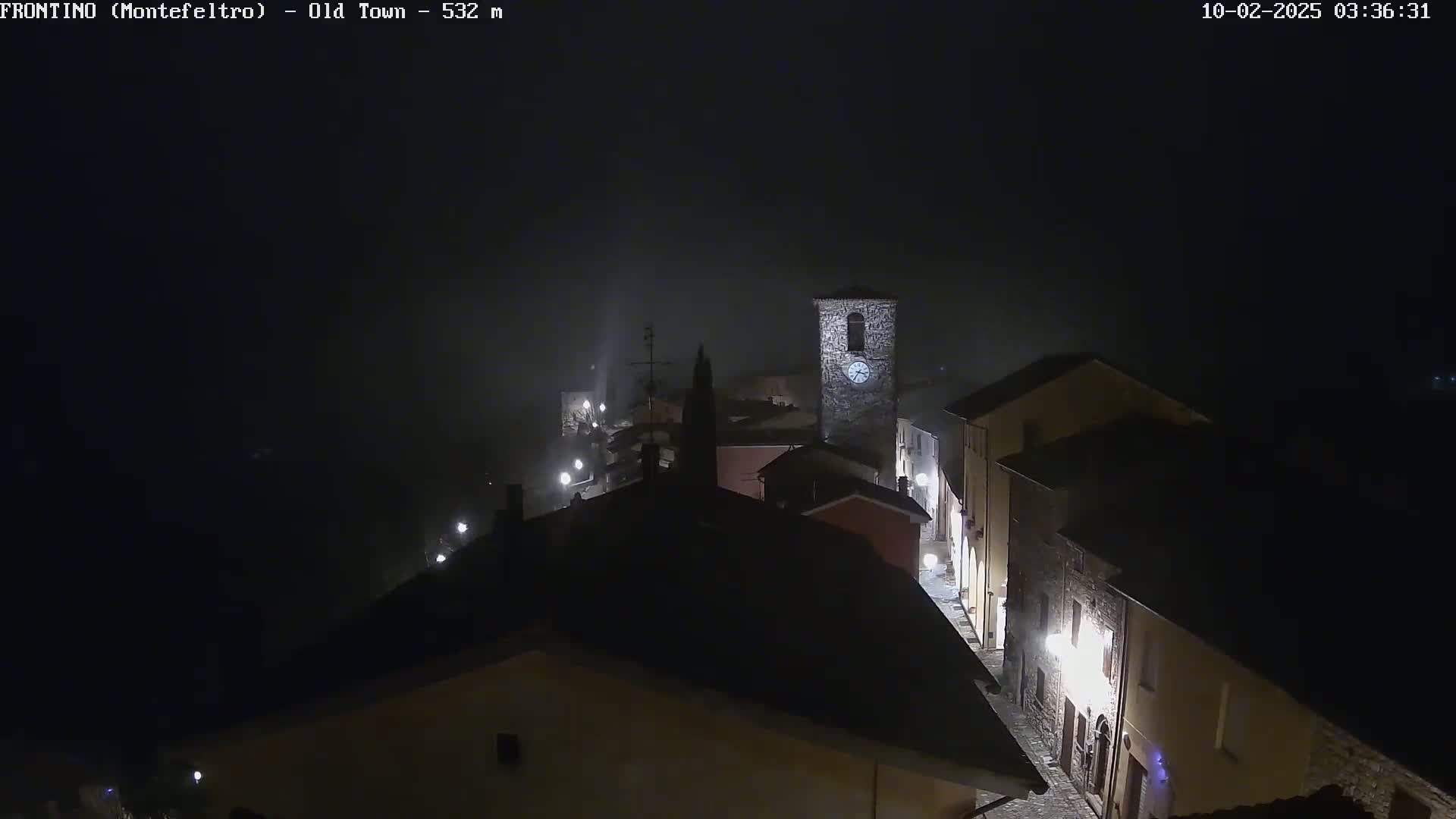 A foggy night scene shows a small town with buildings illuminated by streetlights.