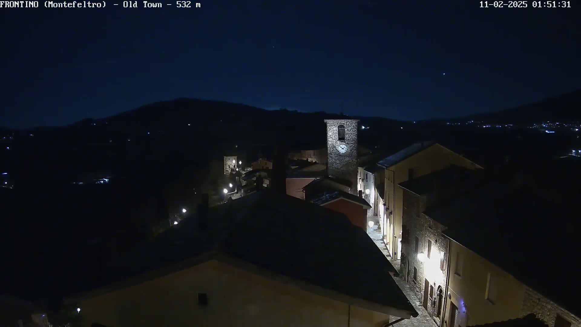 A nighttime, high-angle view shows a small, dark town nestled in a valley under a clear, dark sky.