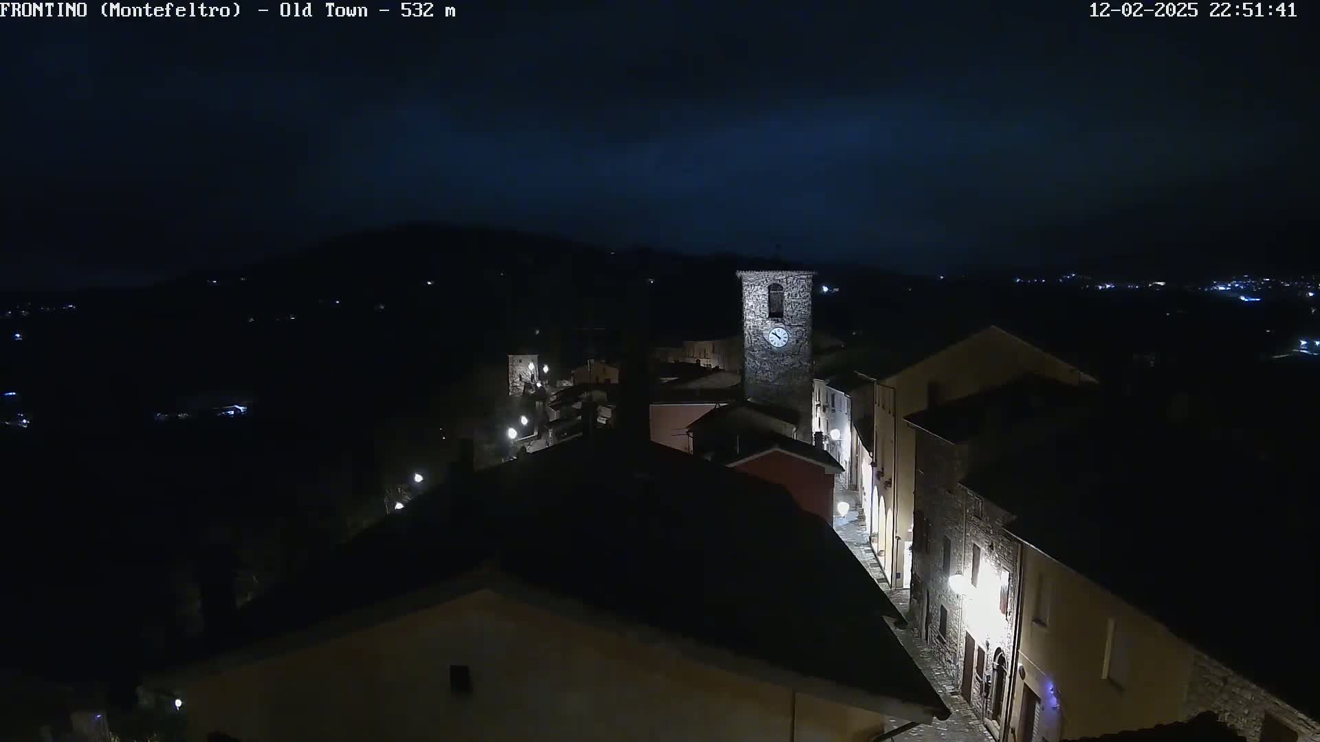 A nighttime, high-angle view of a dimly lit town nestled in a dark landscape under a mostly clear, dark sky.