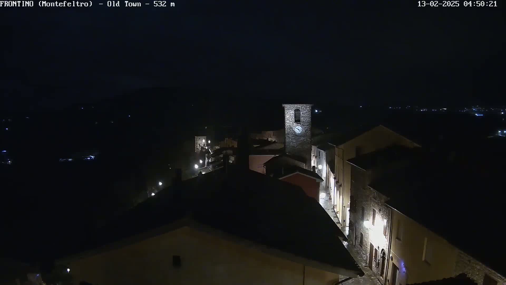 A nighttime aerial view of a small town's old section, illuminated by streetlights, features a prominent clock tower.